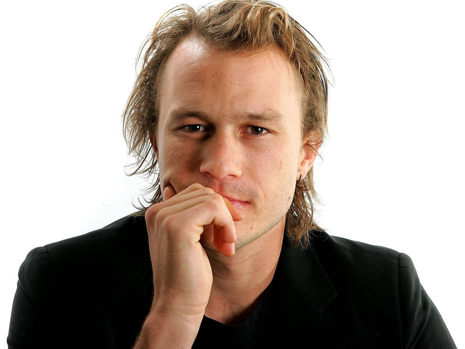Heath Ledger 桌布 壁紙 — 一個頭髮蓬鬆的金髮男子，身穿黑色襯衫，手托下巴，背景是純白色。