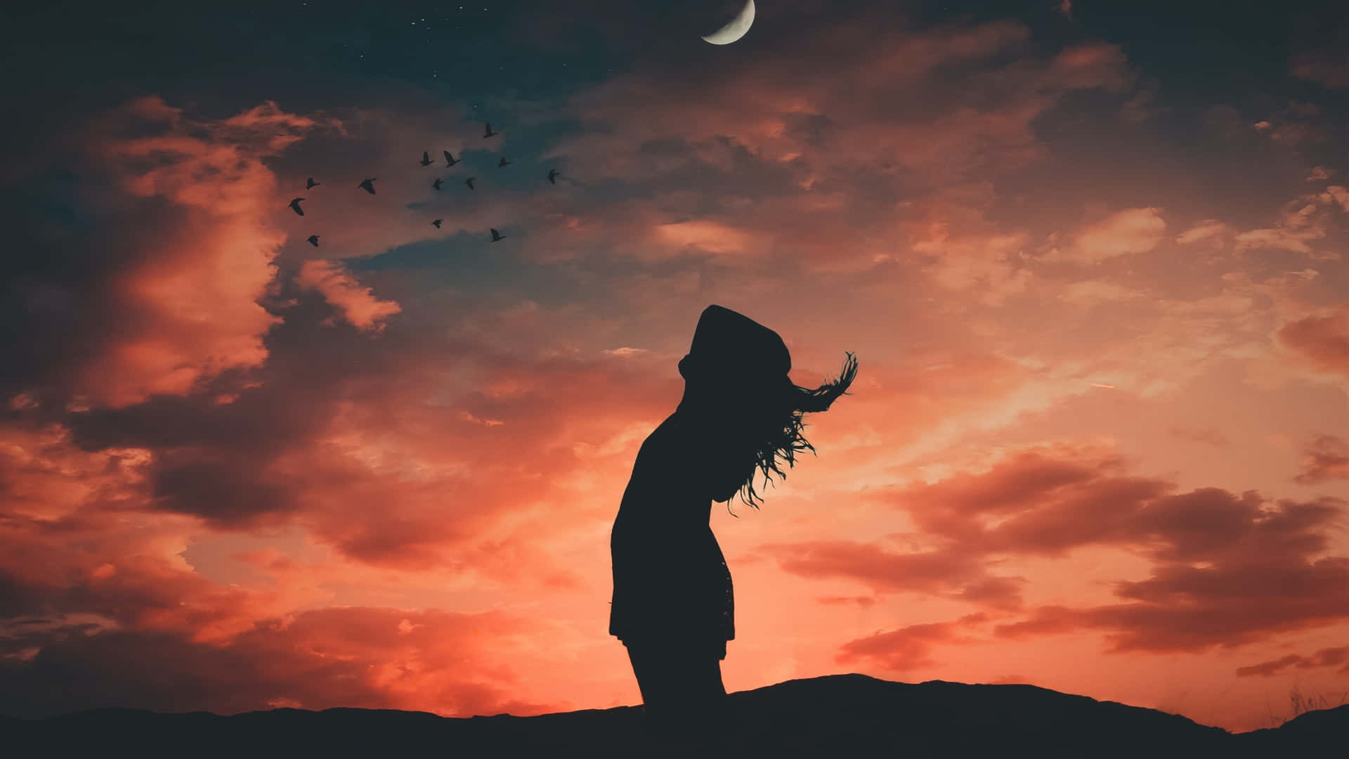 Silhouette 桌布 壁紙 — 一個頭髮飄逸的人站在山頂上的剪影，背景是充滿活力的橙色日落天空，有一彎新月和一群鳥在頭頂飛翔。