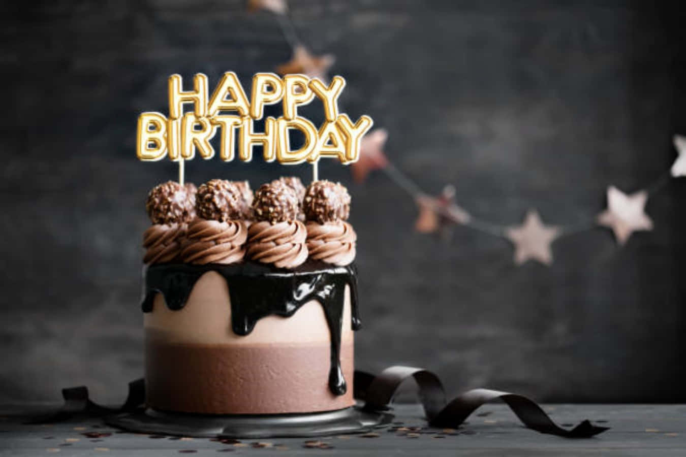 Happy Birthday Cake 桌布 壁紙 — 一個頹廢的巧克力生日蛋糕，帶有金色字母裝飾和星星花環，背景為深色紋理。