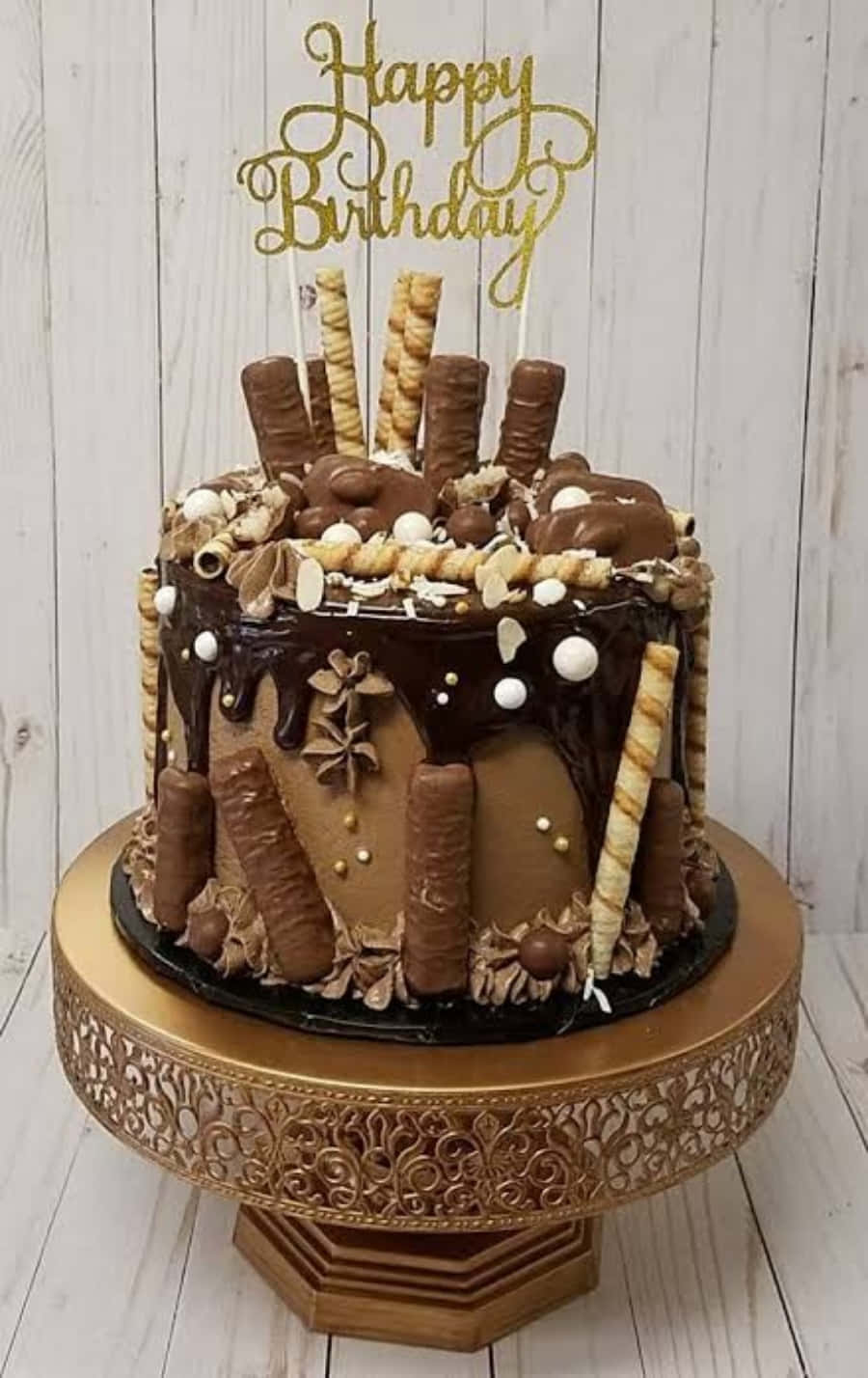 Happy Birthday Cake 桌布 壁紙 — 一個頹廢的巧克力生日蛋糕，飾有糖果棒和金色裝飾，優雅地放在華麗的金色架子上。
