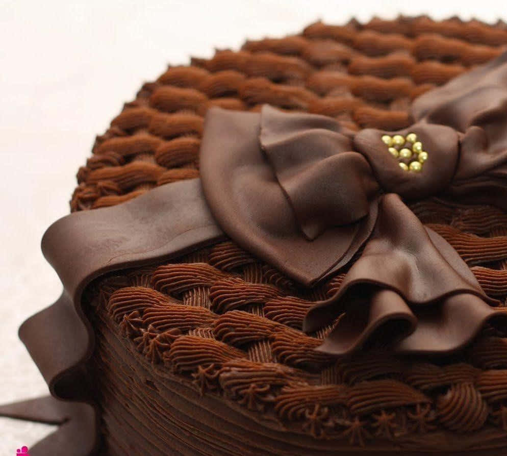 Chocolate Cake 桌布 壁紙 — 一個頹廢的巧克力蛋糕，在質感糖霜表面上飾有光澤的巧克力蝴蝶結和金珠。