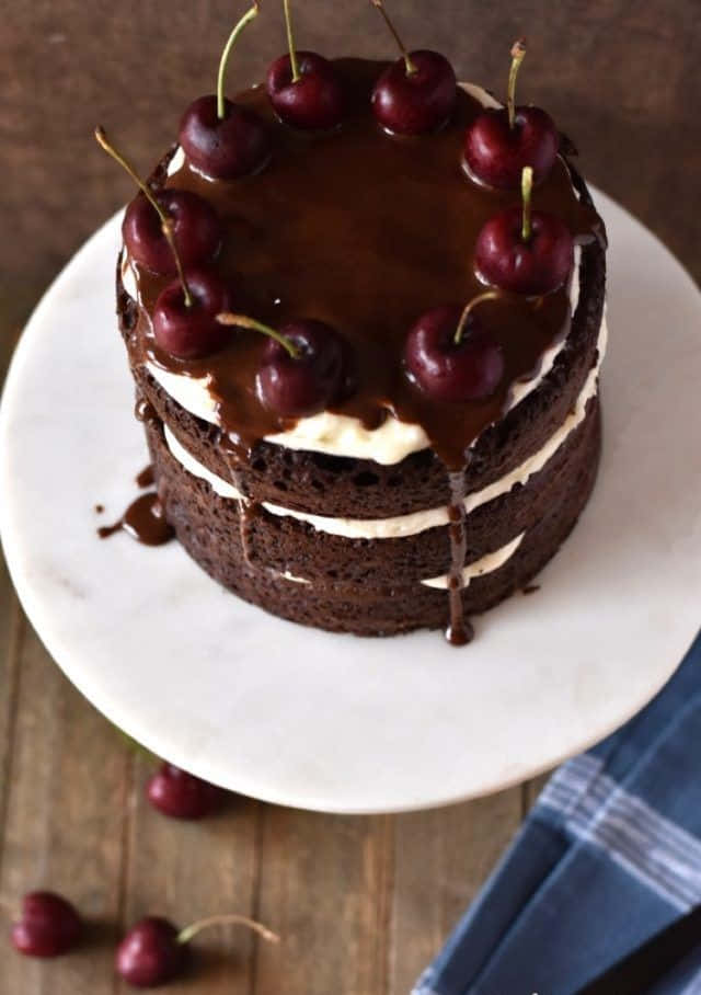 Black Forest Cake 桌布 壁紙 — 一個頹廢的巧克力蛋糕，帶有白色奶油層和光澤的櫻桃，在大理石架上滴著巧克力醬。