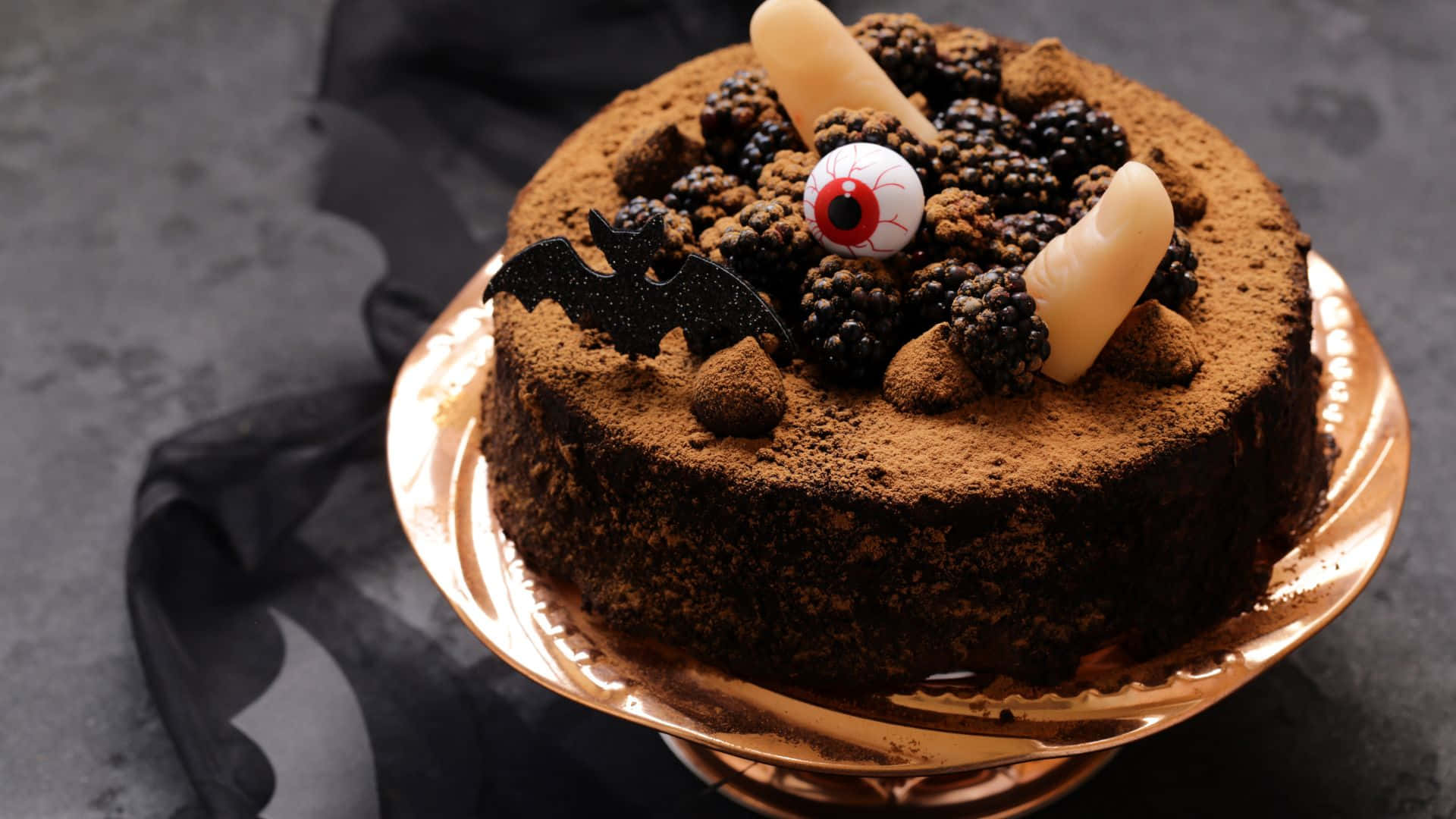 Halloween Cake 桌布 壁紙 — 一個頹廢的巧克力蛋糕，撒上可可粉，上面放有黑莓、假手指和一個金架上的凸眼。