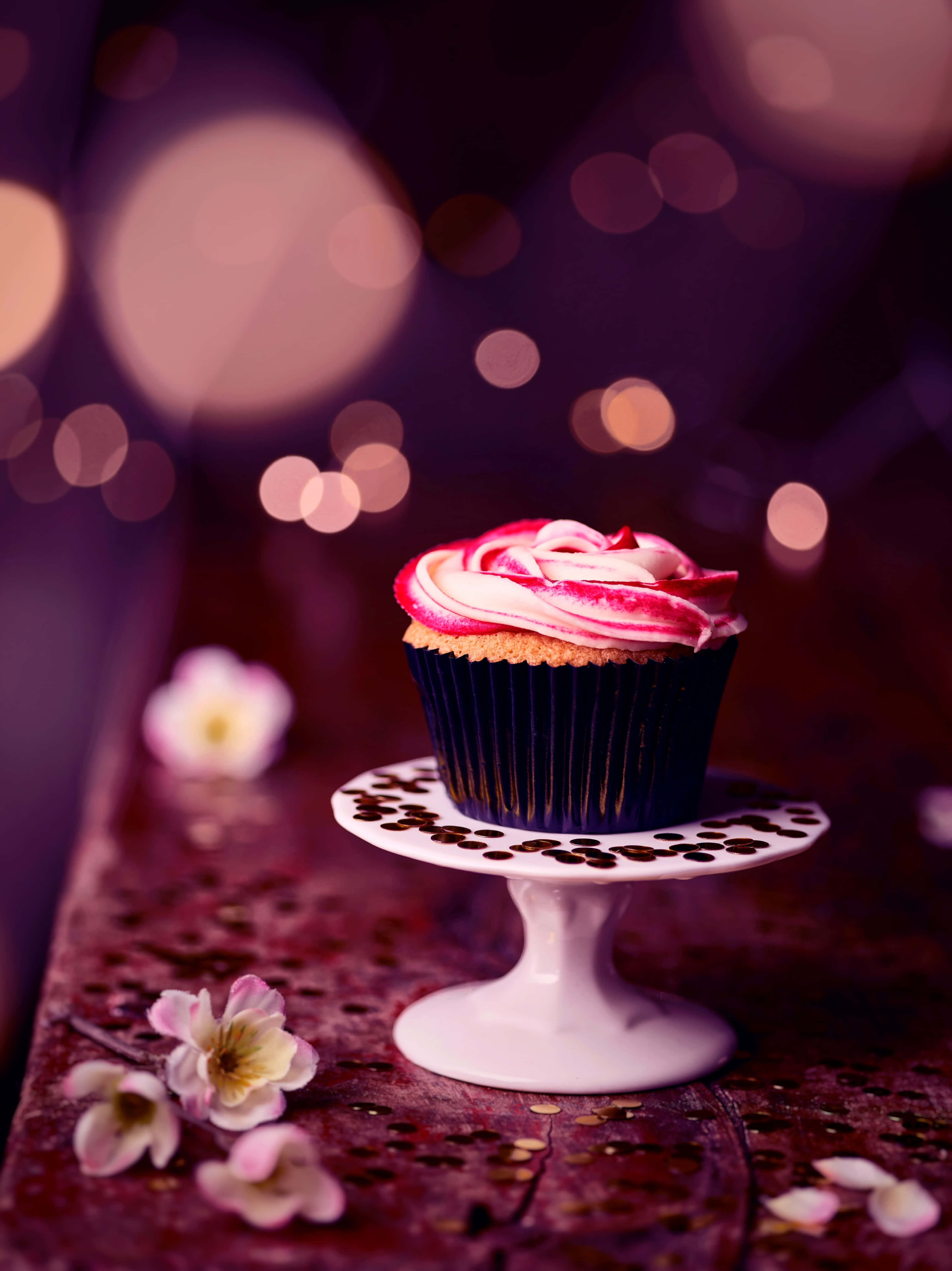 Cupcake 桌布 壁紙 — 一個頹廢的杯子蛋糕，帶有粉紅色和白色糖霜漩渦，優雅地放在白色底座上，背景是夢幻的紫色散景。