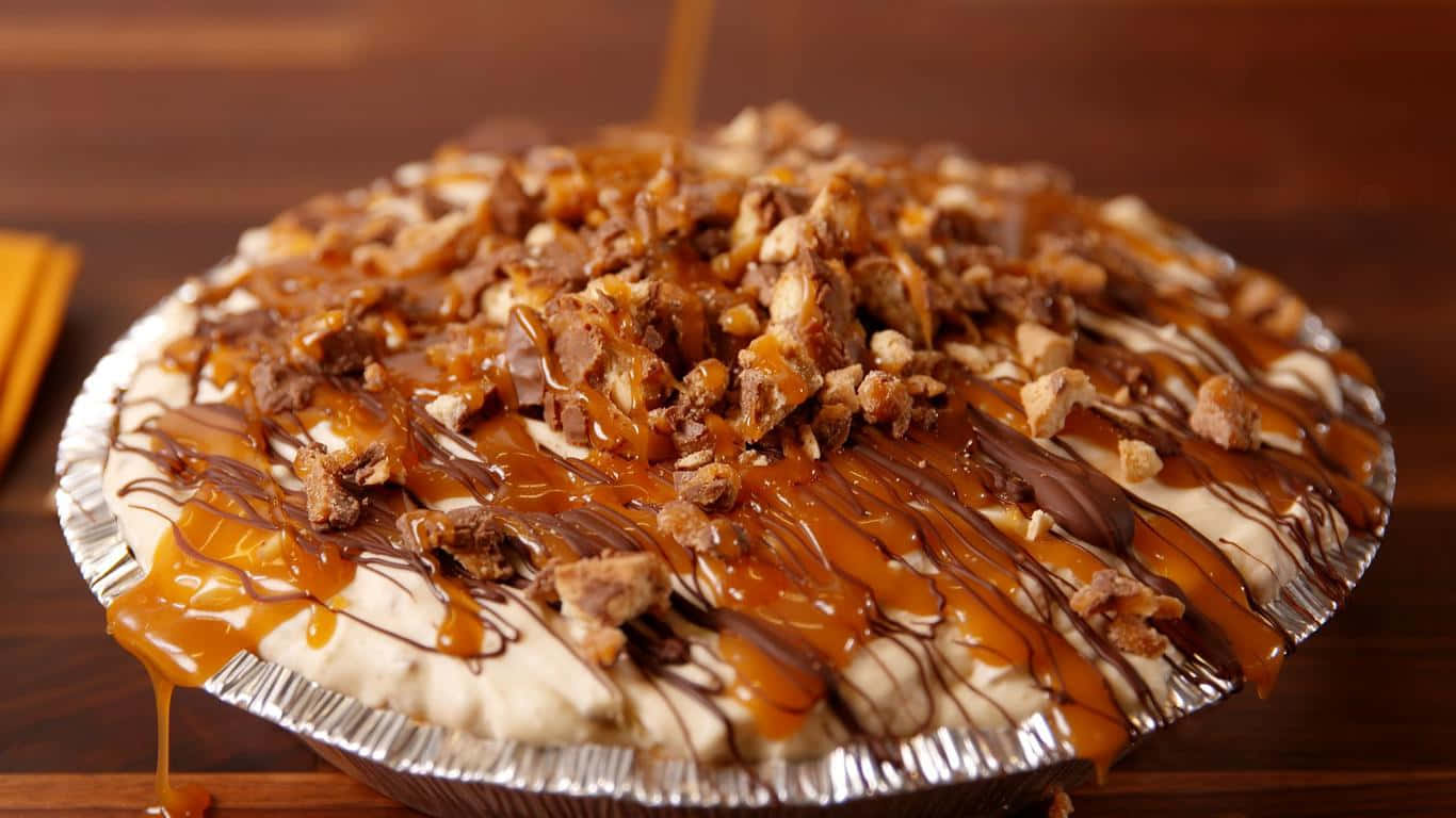 1366x768 Desserts 桌布 壁紙 — 一個頹廢的焦糖淋餡餅，上面撒有切碎的糖果棒和融化的醬汁，放在錫箔盤中。