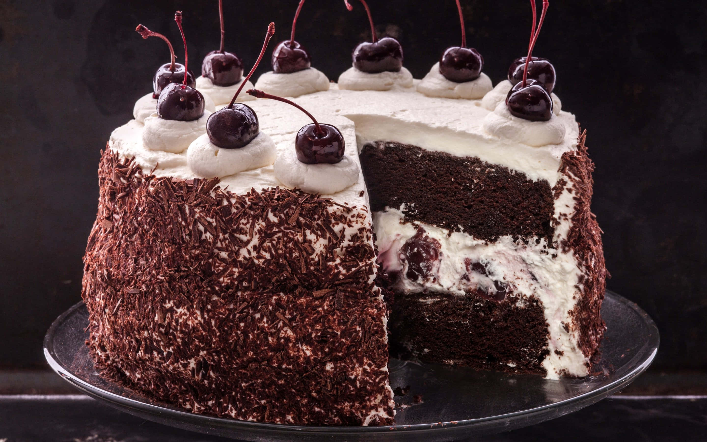 Black Forest Cake 桌布 壁紙 — 一個頹廢的黑森林蛋糕，上面有巧克力碎和櫻桃，放在玻璃盤上，其中一塊已被切走。