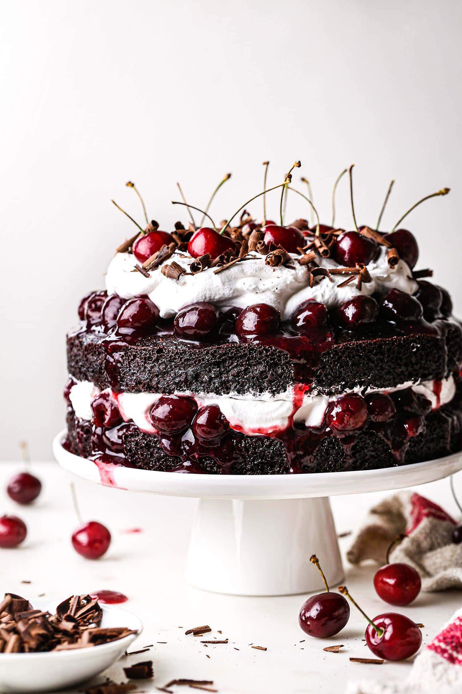 Black Forest Cake 桌布 壁紙 — 一個頹廢的黑森林蛋糕，層層疊疊的巧克力海綿蛋糕、奶油和櫻桃，放在白色架子上。