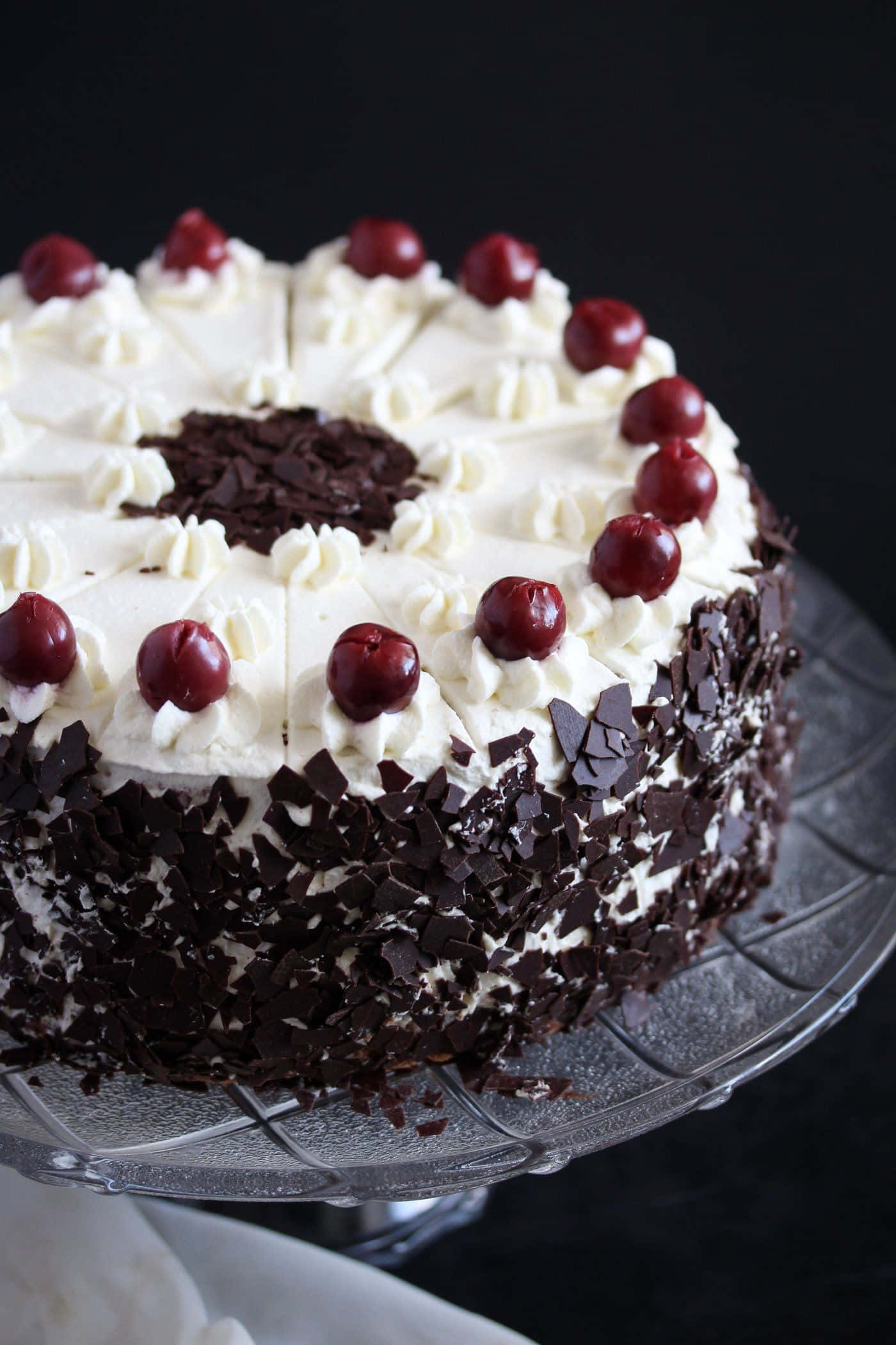 Black Forest Cake 桌布 壁紙 — 一個頹廢的黑森林蛋糕，飾以鮮奶油、巧克力刨花和光亮的櫻桃，置於玻璃架上。