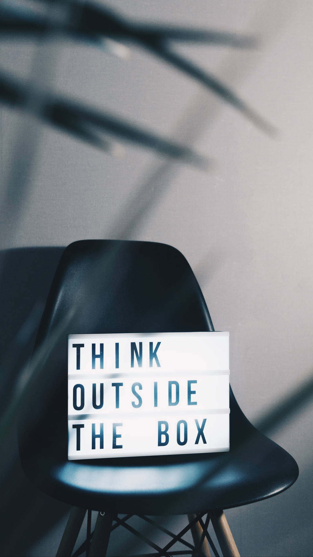 黑色椅子上的燈箱寫著 think outside the box，在牆上投射陰影 — Note 10 Plus 壁紙