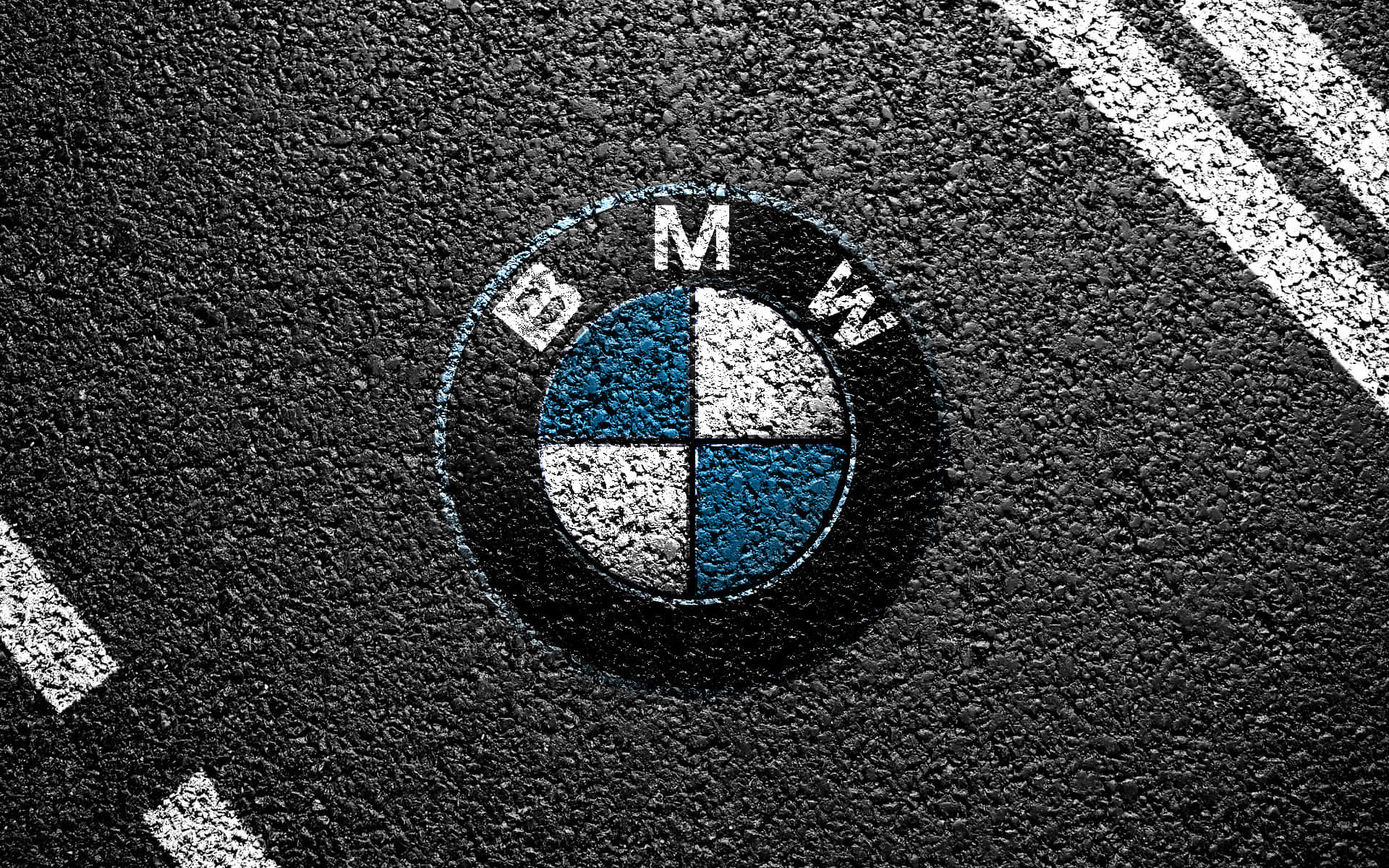 Bmw Logo 桌布 壁紙 — 一個風化的BMW標誌畫在粗糙的瀝青上，附近有白色道路標線彎曲。