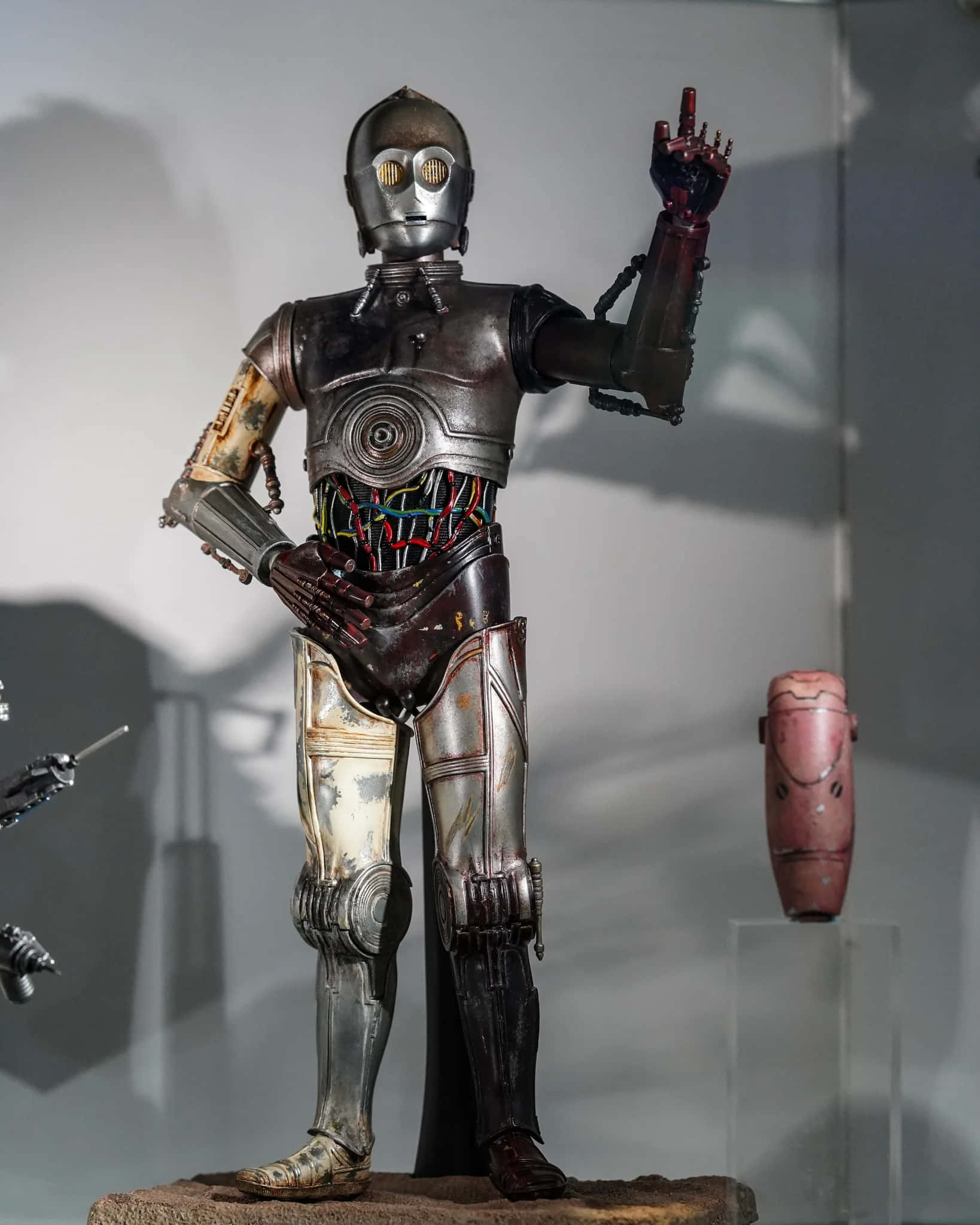 C-3po 桌布 壁紙 — 一個風化的C-3PO機器人雕像在博物館燈光下展出，帶有外露的電線和生鏽的金屬部件。