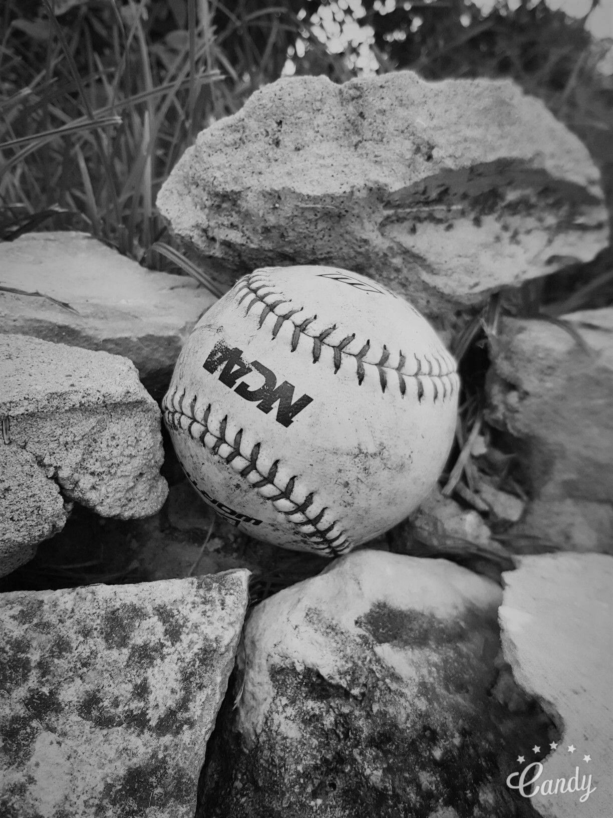 Cute Softball 桌布 壁紙 — 一個風化的NCAA壘球在單色戶外場景中躺在粗糙的石頭之間。