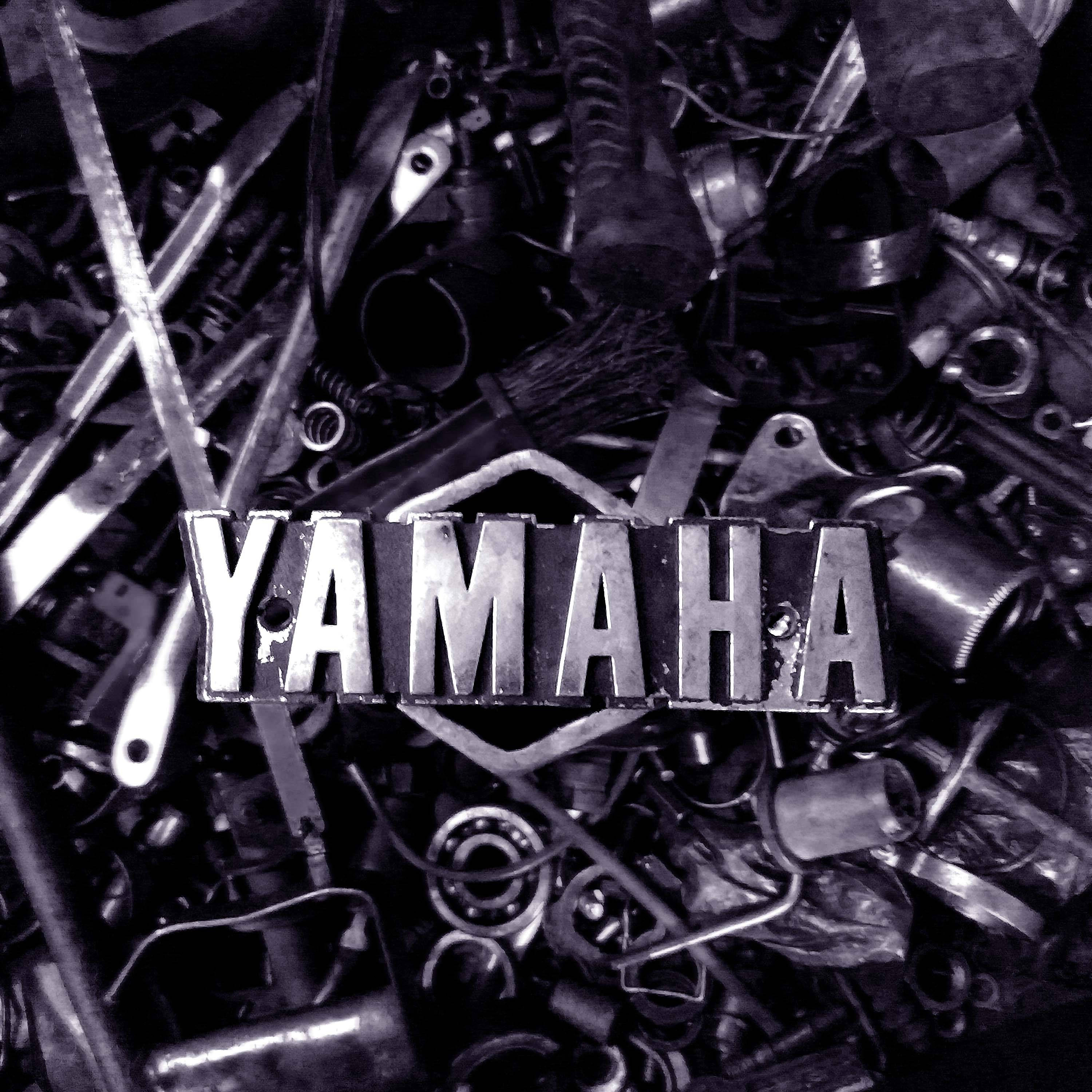 Rx100 桌布 壁紙 — 一個風化的Yamaha標誌從一堆混亂的金屬機車零件中浮現，呈現單色調。