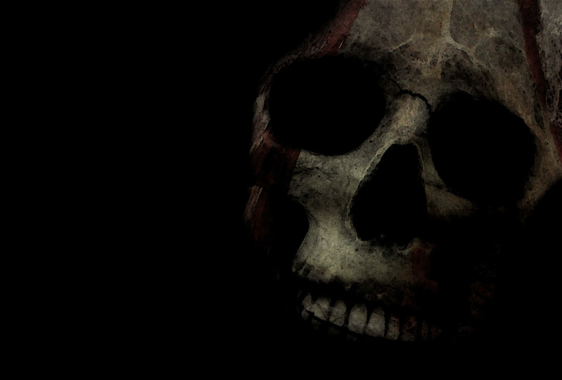 Black Skeleton 桌布 壁紙 — 一個風化的人類頭骨帶有紅色標記，在漆黑的背景下隱約發光。