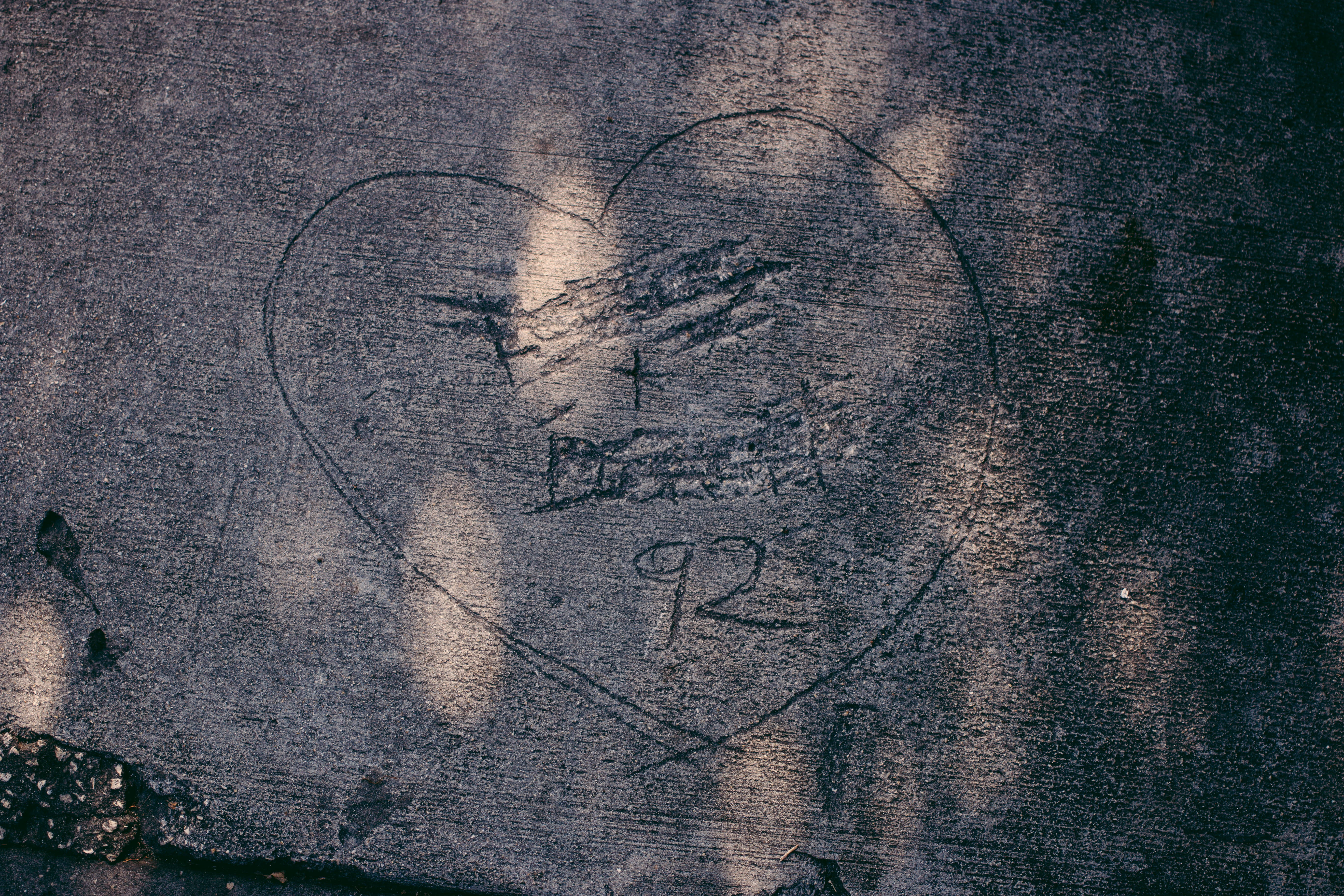 Relationship 桌布 壁紙 — 一個風化的心形刻在粗糙的混凝土上，帶有褪色的縮寫和數字92，在斑駁的陽光下。