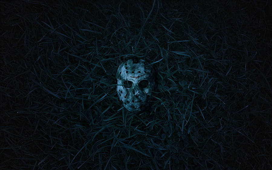 桌布 壁紙 — 一個風化的曲棍球面具在陰森藍光下躺在暗草中，喚起恐怖與懸念。