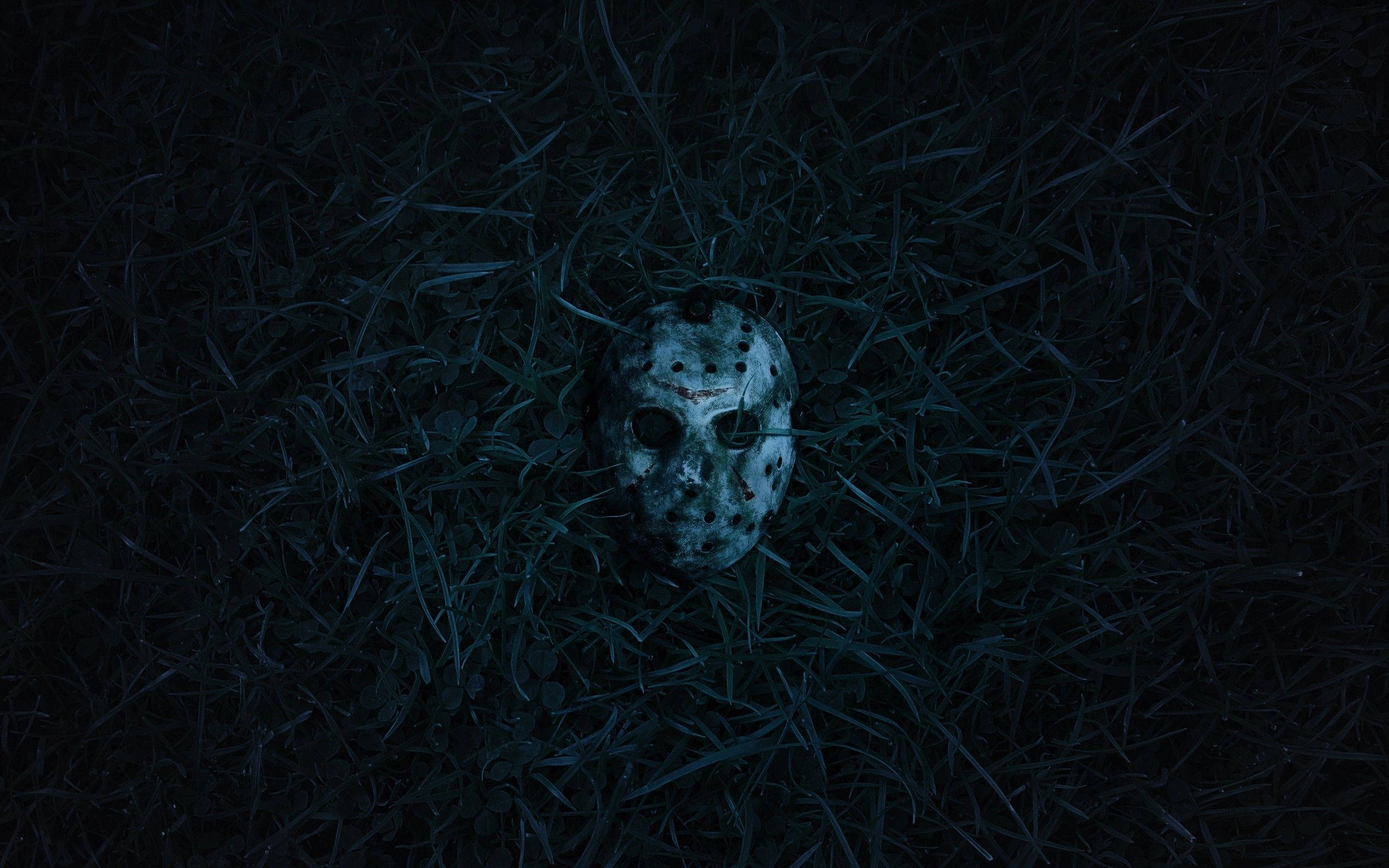 jason 桌布 壁紙 — 一個風化的曲棍球面具躺在暗色草地上，在昏暗的藍色燈光下營造出令人毛骨悚然的恐怖氛圍。