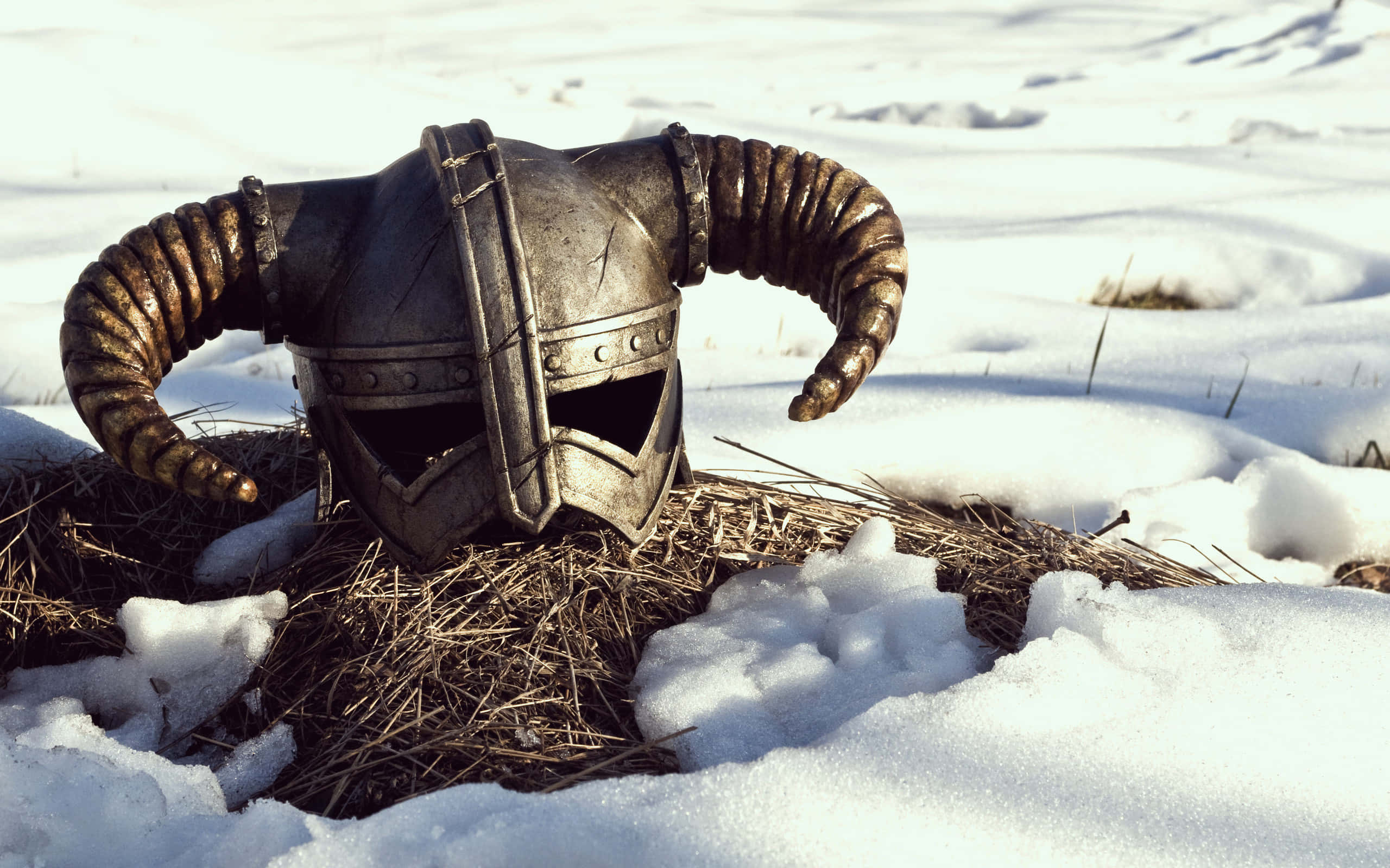 dovahkiin 桌布 壁紙 — 一個風化的有角頭盔在明亮的陽光下，放在雪地裡的乾草捆上。