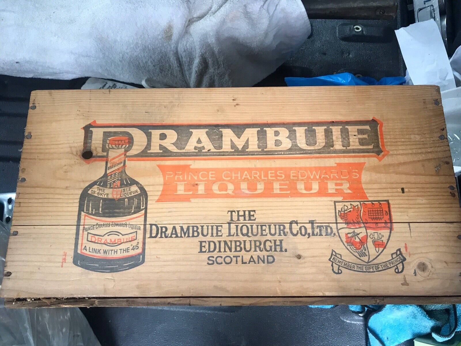 復古 桌布 壁紙 — 一個風化的木箱，帶有復古的「Drambuie Liqueur」品牌和蘇格蘭紋章，放置在雜亂的工作室物品中。