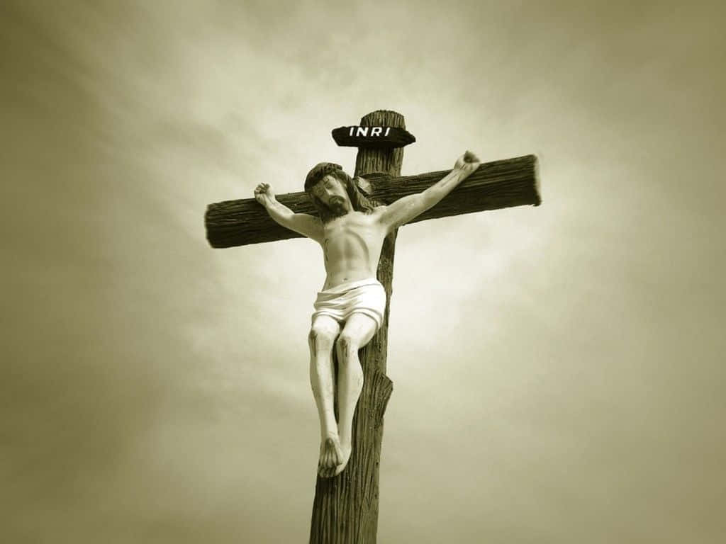 Jesus Crucifixion 桌布 壁紙 — 一個風化的木製十字架，上面有雕刻的耶穌像，背景是陰沉的雲天。