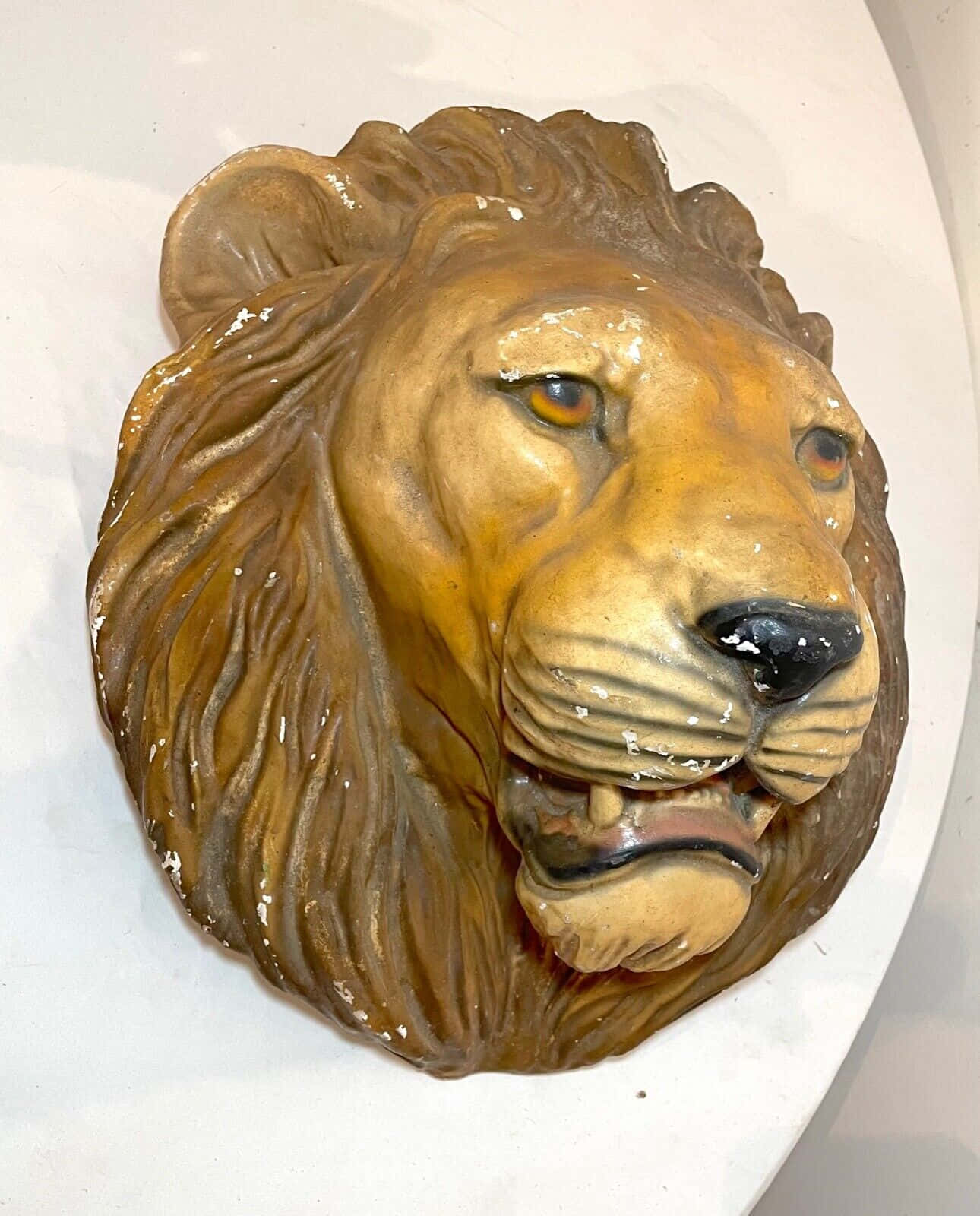 Lion Head 桌布 壁紙 — 一個風化的獅子頭雕塑，帶有細緻的鬃毛和琥珀色眼睛，安裝在白色牆上。