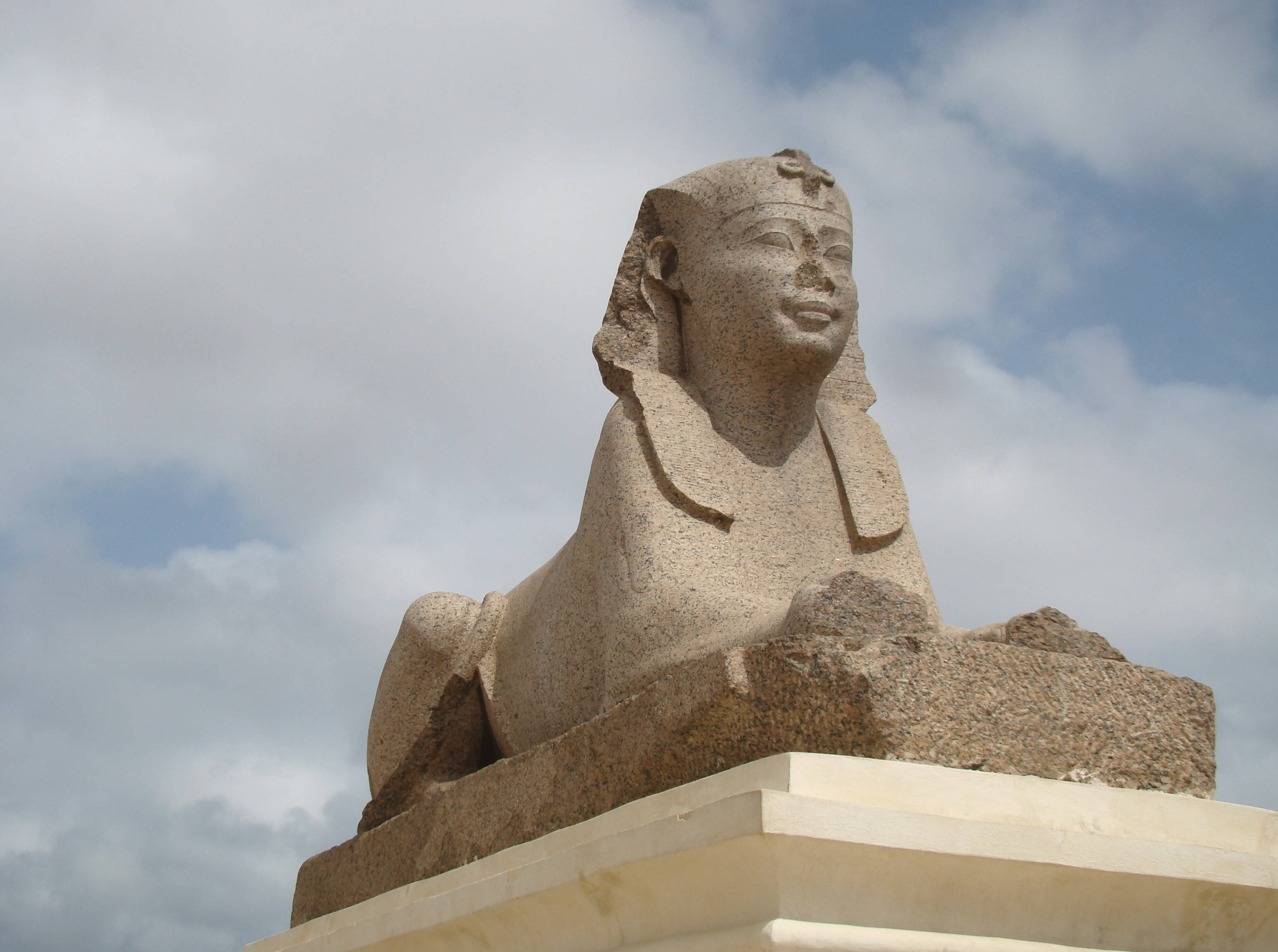 Alexandria 桌布 壁紙 — 一個風化的石獅身人面像，有人頭和獅身，坐在基座上，天空多雲。