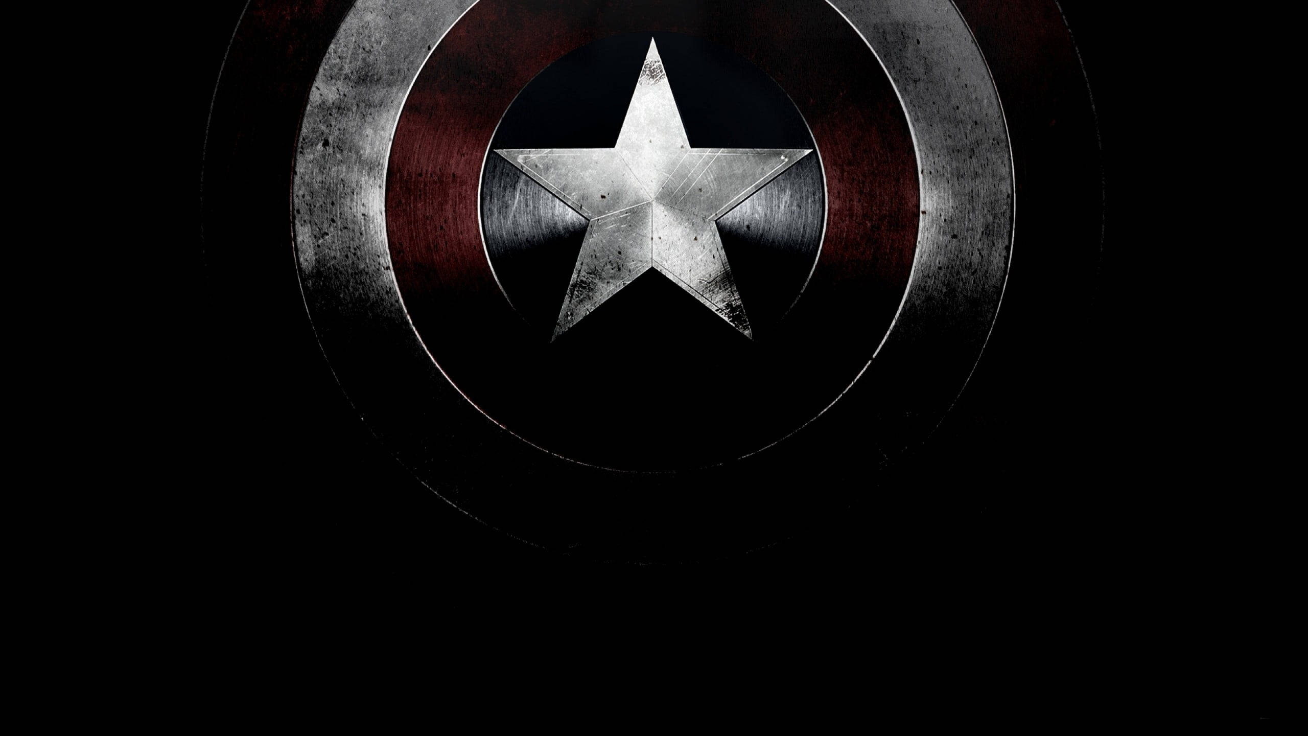 Marvel Captain America 桌布 壁紙 — 一個風化的美國隊長盾牌，中心有星星，在黑色背景上發光。
