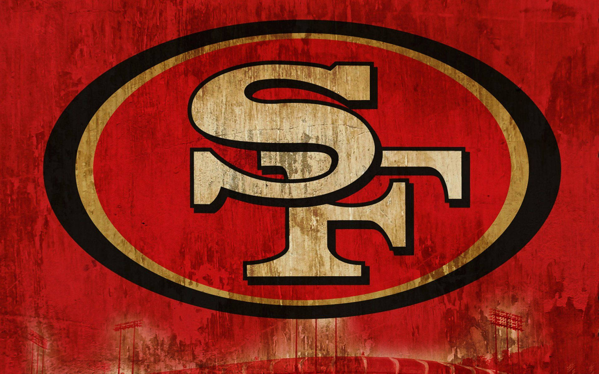 49ers 桌布 壁紙 — 一個風化的舊金山49人隊標誌，帶有磨損的紅色、金色和黑色，在紋理背景上。
