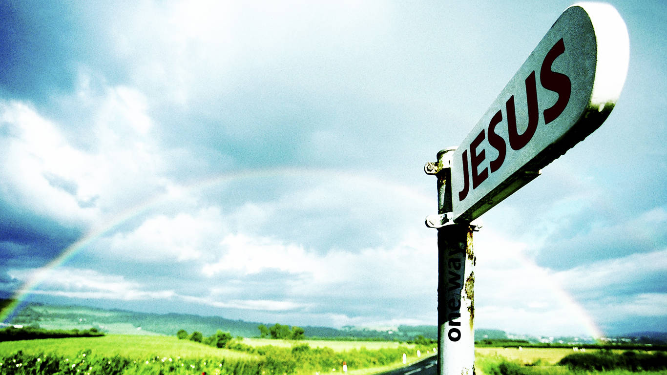 耶穌 桌布 壁紙 — 一個風化的路牌寫著「JESUS」，立在綠色田野中，天空多雲，背後有一道淡淡的彩虹。
