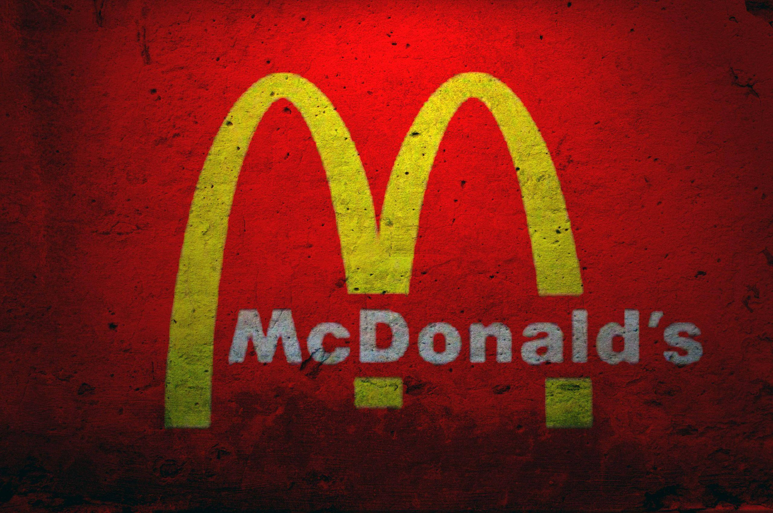 Mcdonalds 桌布 壁紙 — 一個風化的麥當勞標誌，黃色拱門和白色文字在紋理紅色背景上。