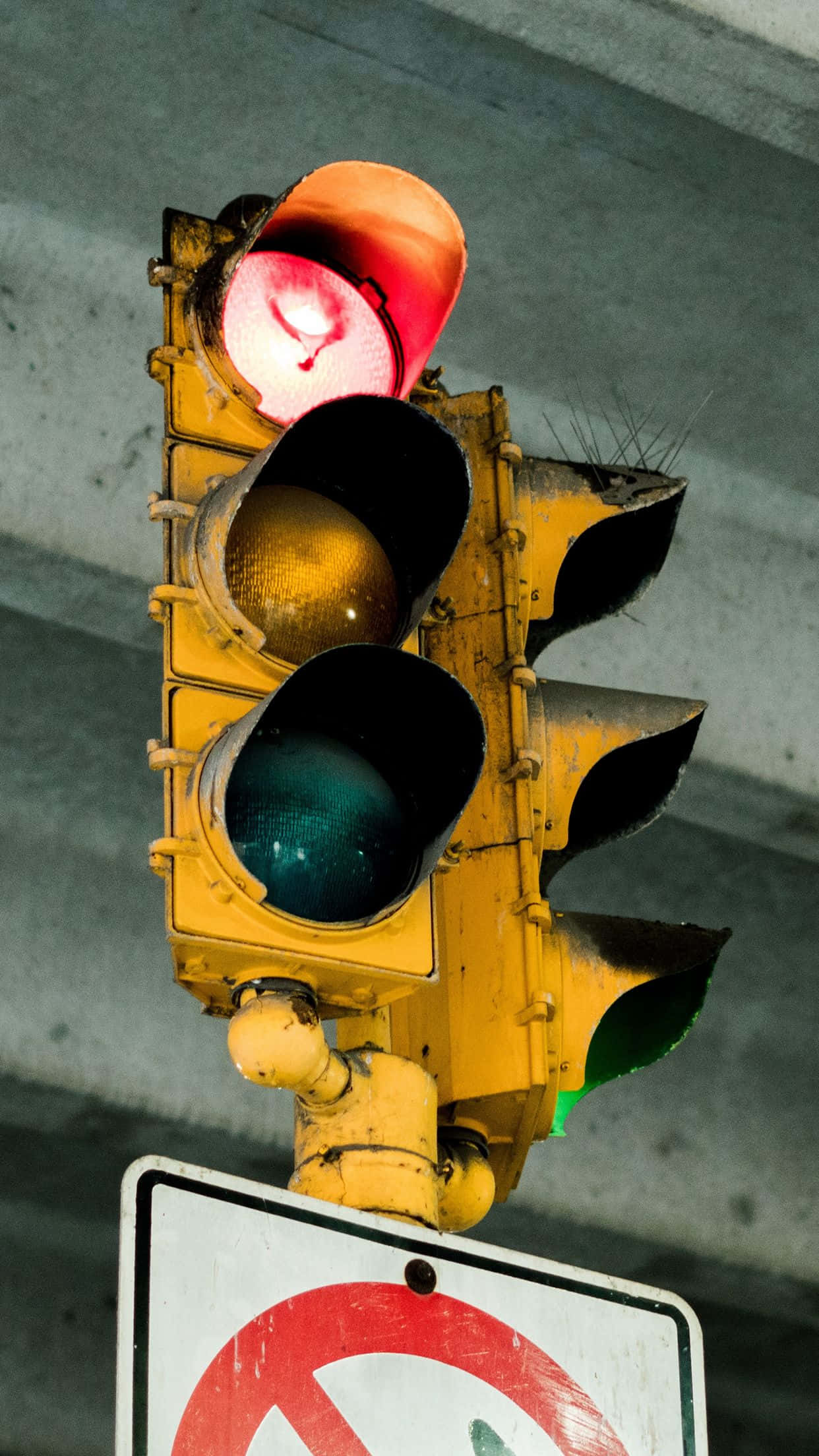 Stop Light 桌布 壁紙 — 一個風化的黃色交通號誌，頂部亮著紅燈，懸掛在混凝土高架橋下。