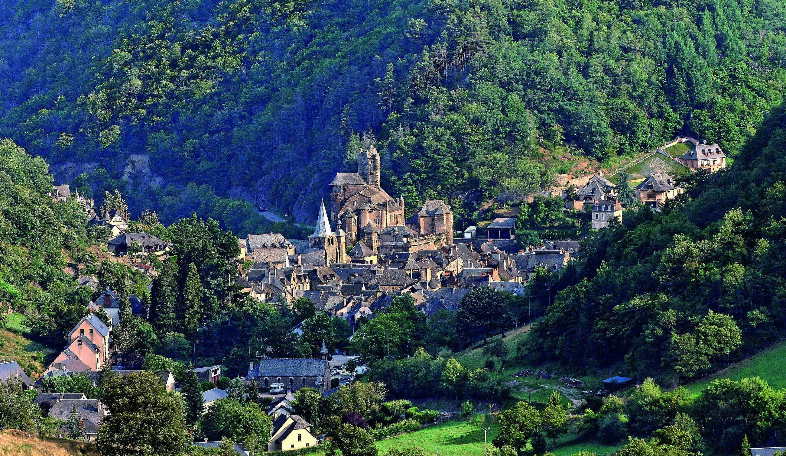 France 桌布 壁紙 — 一個風景如畫的中世紀村莊，坐落在鬱鬱蔥蔥的綠色山丘中，擁有石頭建築和一座突出的教堂。