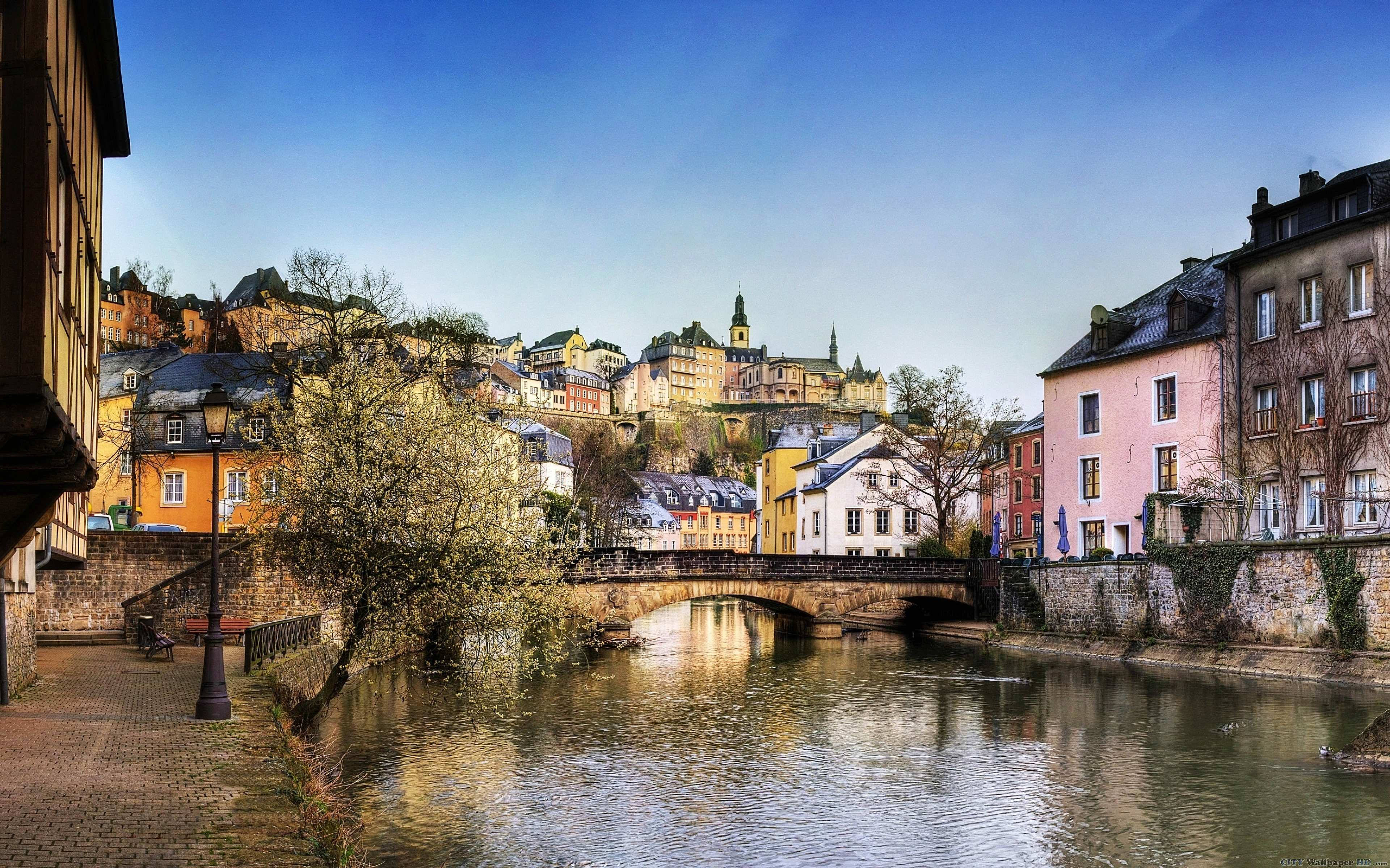 Luxembourg 桌布 壁紙 — 一個風景如畫的歐洲河畔小鎮，擁有色彩繽紛的歷史建築和一座石橋，在清澈的藍天下。