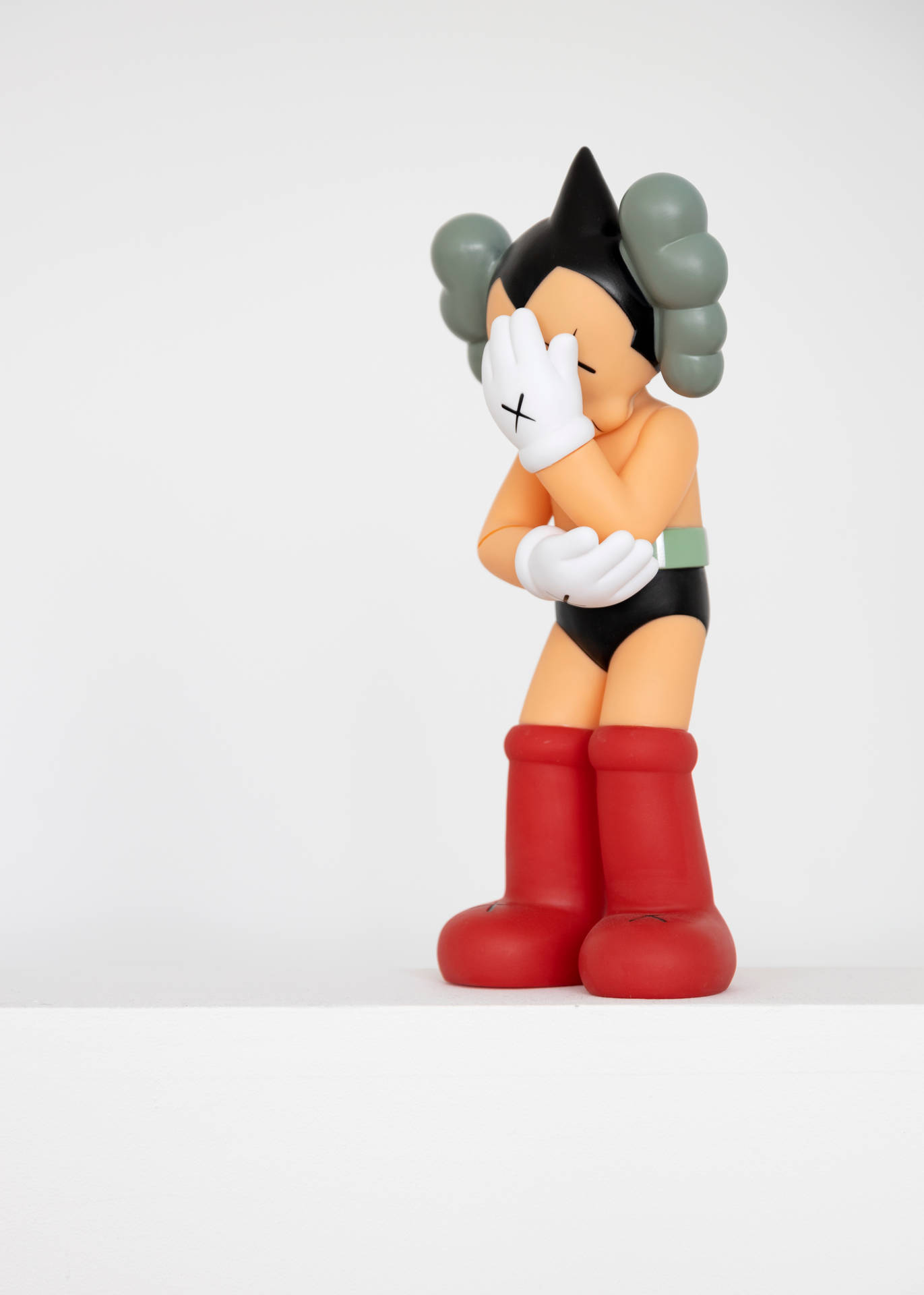 kaws pc 桌布 壁紙 — 一個風格化的原子小金剛公仔，灰色雲狀頭髮，紅色靴子，站在純白色背景前，用一隻戴手套的手遮住臉。