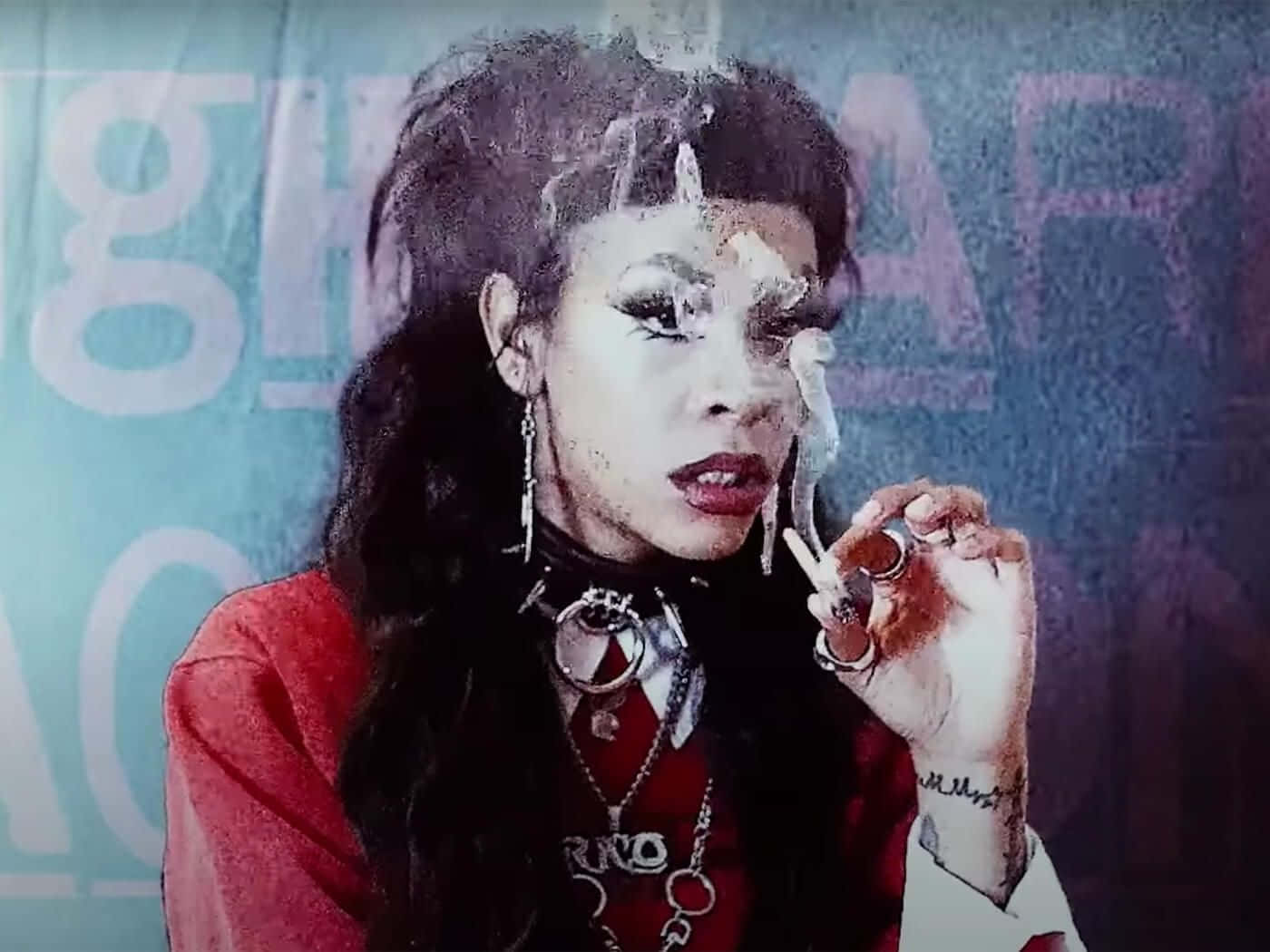 Rico Nasty 桌布 壁紙 — 一個風格化的女性肖像，深色頭髮和鮮豔妝容，手持香煙，背景為帶有褪色文字的紋理藍色背景。