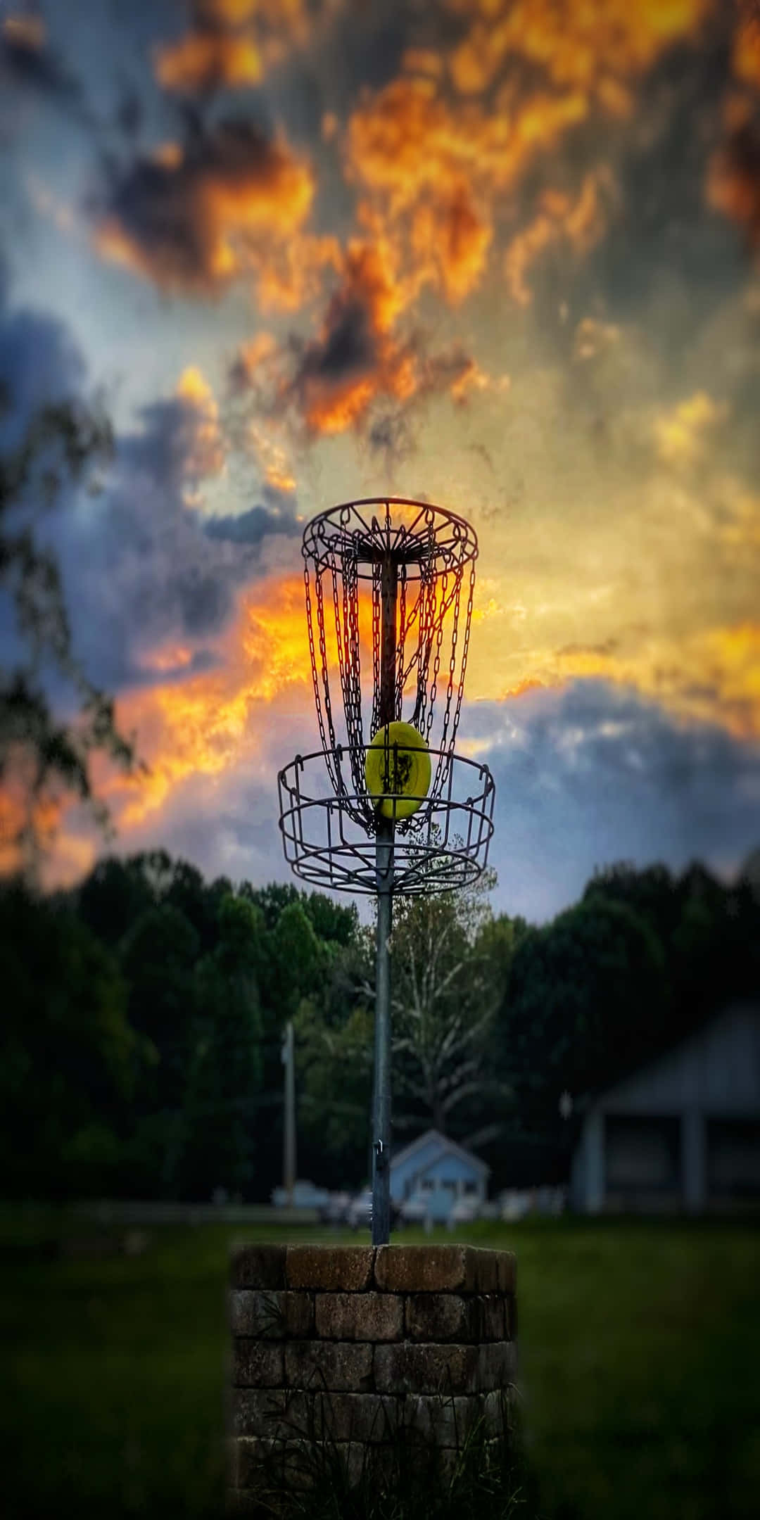 Pixel 3 Frisbee 桌布 壁紙 — 一個飛盤高爾夫籃筐在戲劇性的雲層映襯下，於熾熱的日落天空中托著一個亮黃色的飛盤。