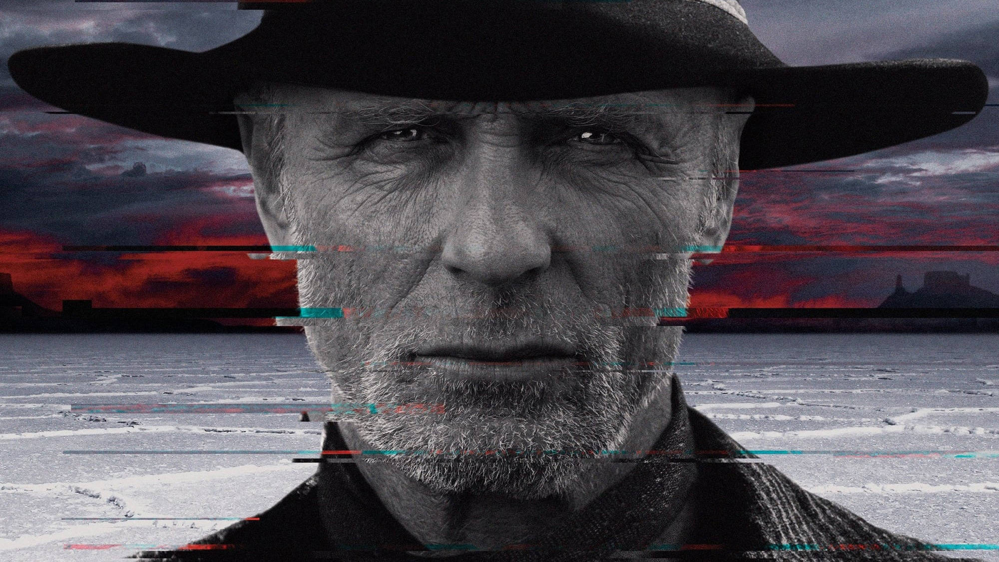 Westworld 桌布 壁紙 — 一個飽經風霜、戴著黑色帽子的男人，在一個帶有火紅日落天空的故障沙漠背景下強烈凝視。