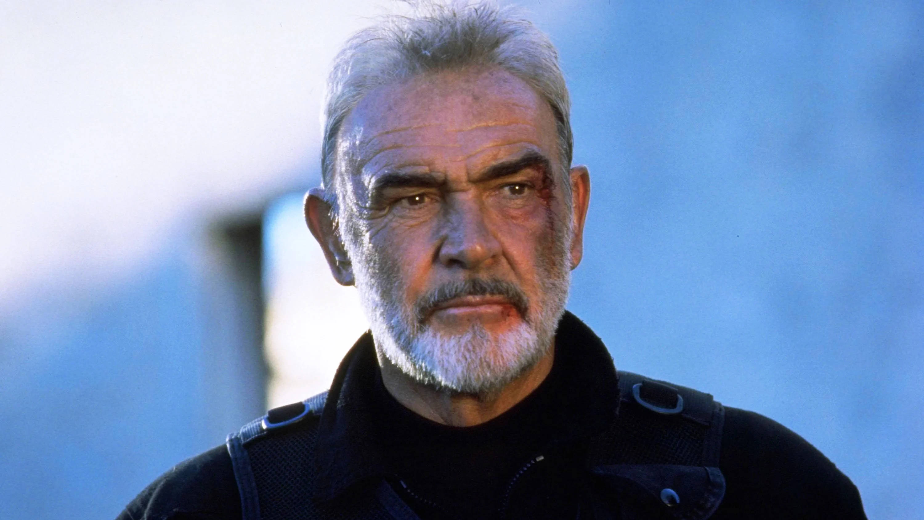 Sean Connery 桌布 壁紙 — 一個飽經風霜、灰白頭髮的男人，用一隻血淋淋的眼睛，在模糊的藍色背景前凝視著。
