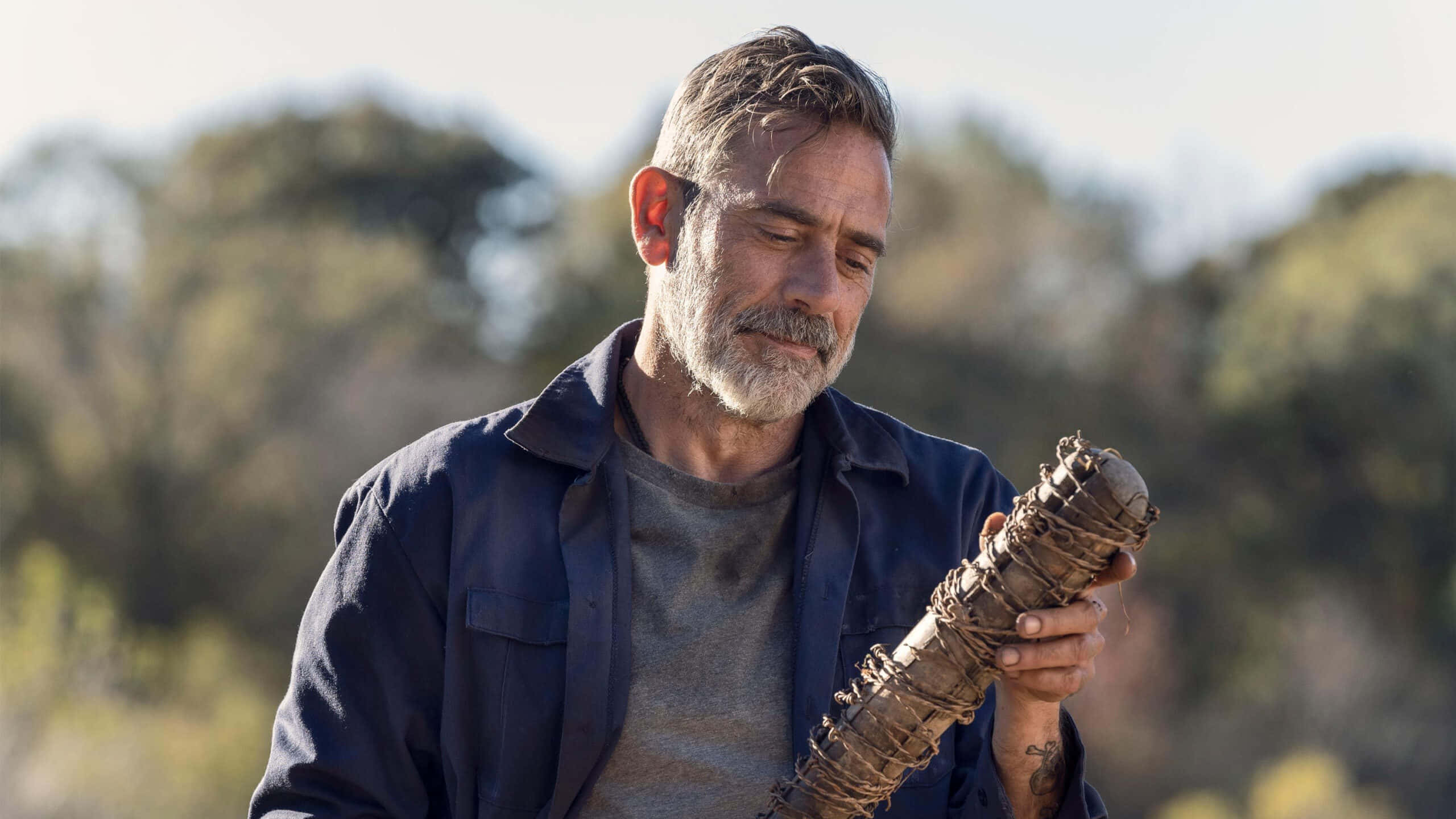 jeffrey dean morgan 桌布 壁紙 — 一個飽經風霜、留著灰色鬍鬚的男人在明亮的日光下於戶外手持簡陋武器。