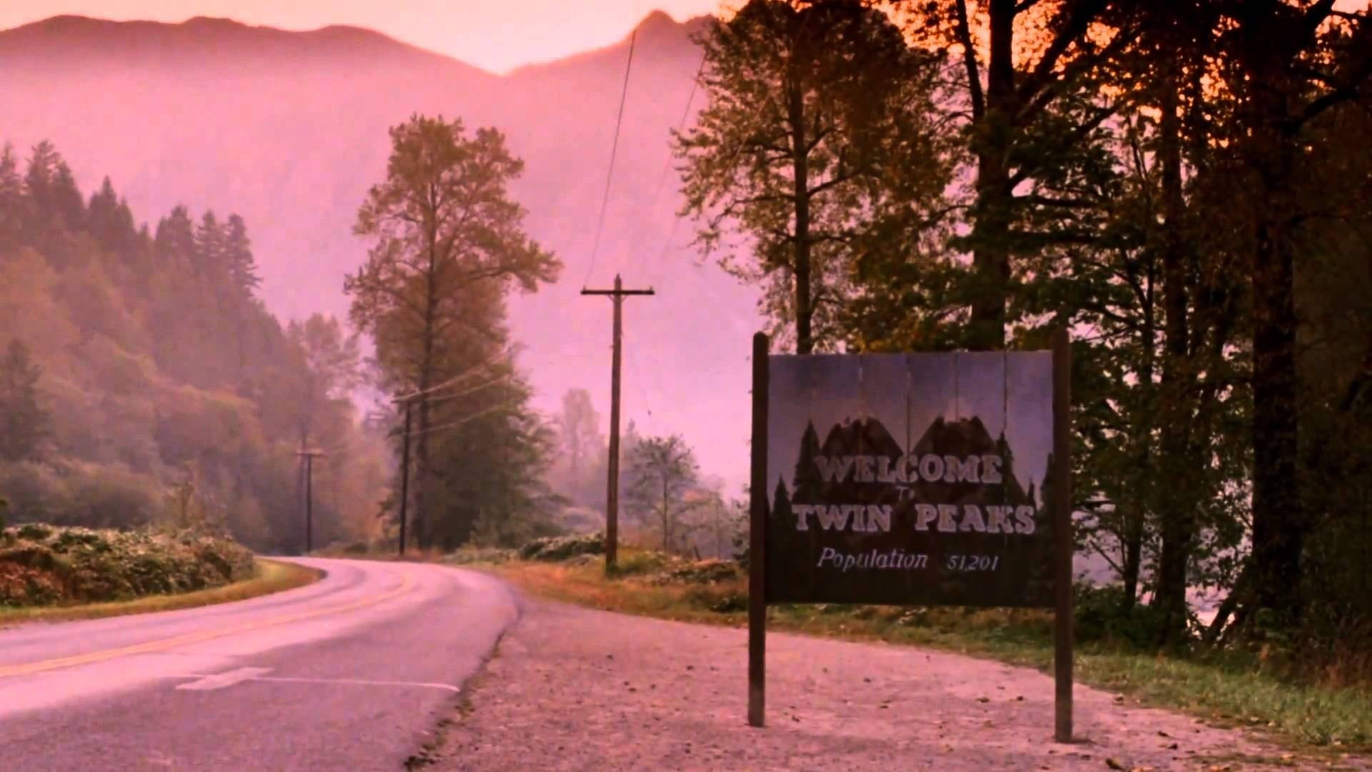 美學 桌布 壁紙 — 一個飽經風霜的 Twin Peaks 歡迎牌矗立在黎明時分蜿蜒穿過霧氣瀰漫的松樹林的道路邊緣。
