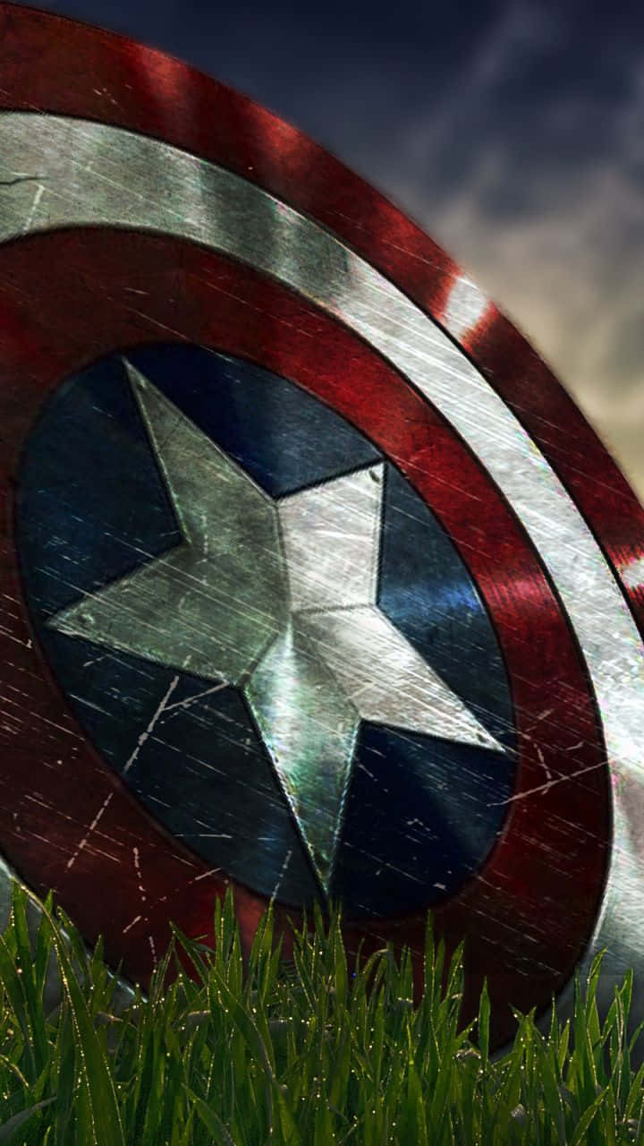 Captain America Android 桌布 壁紙 — 一個飽經風霜的美國隊長盾牌擱在沾滿露水的綠草上，天空多雲。