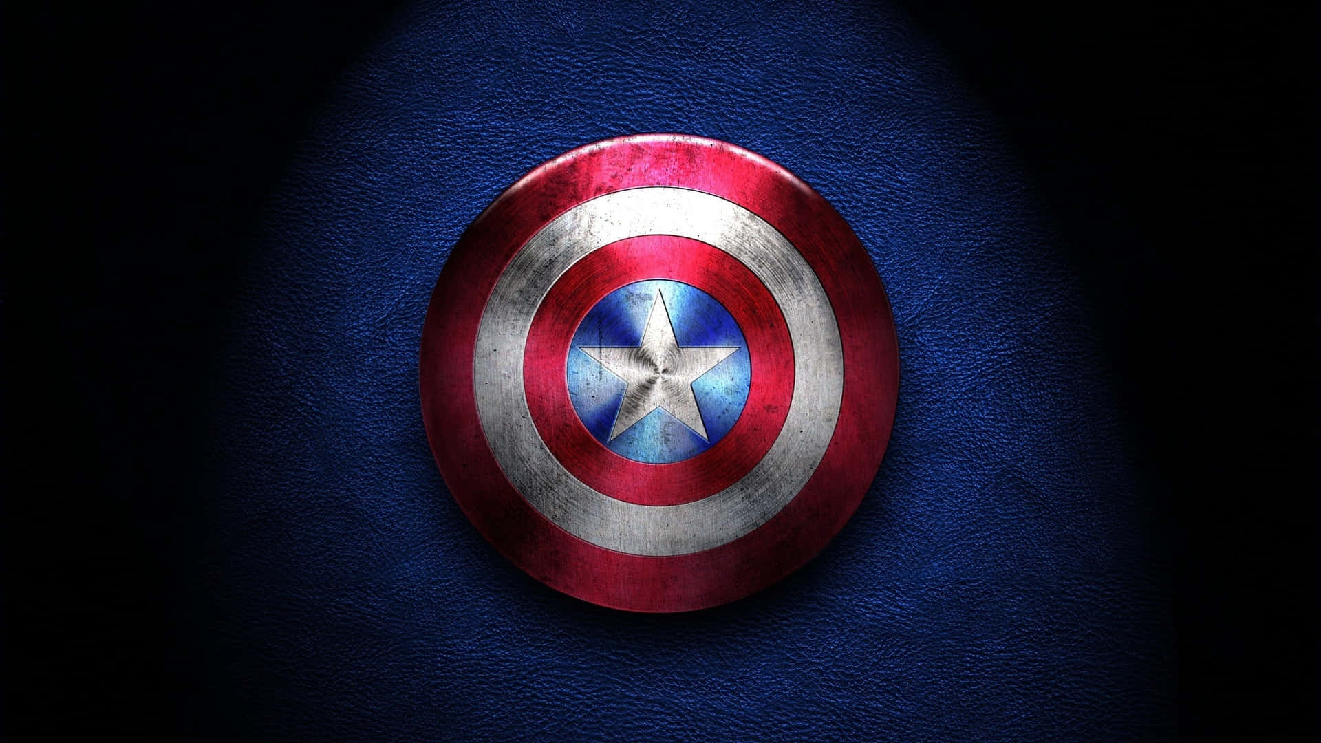 Captain America Cool 桌布 壁紙 — 一個飽經風霜的美國隊長盾牌放置在帶有紋理的藍色表面上，在戲劇性的聚光燈下。