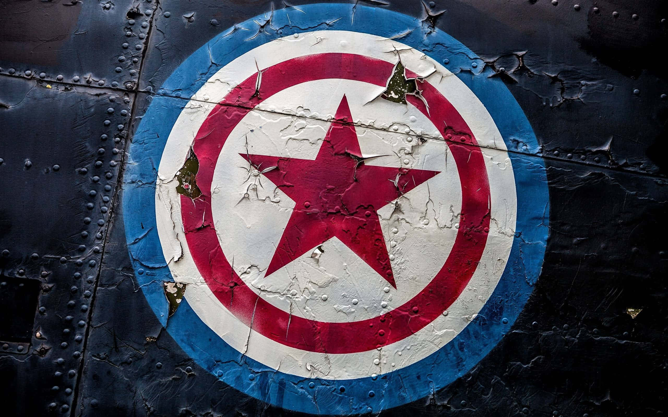 Captain America Logo 桌布 壁紙 — 一個飽經風霜的美國隊長盾牌標誌從鉚接的深色金屬飛機機身上剝落。