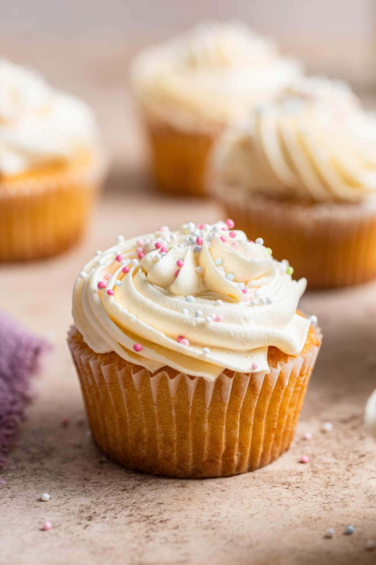 Cupcake 桌布 壁紙 — 一個香草紙杯蛋糕的特寫，帶有奶油糖霜和粉彩糖粒，處於焦點，而其他蛋糕在背景中柔和地模糊。