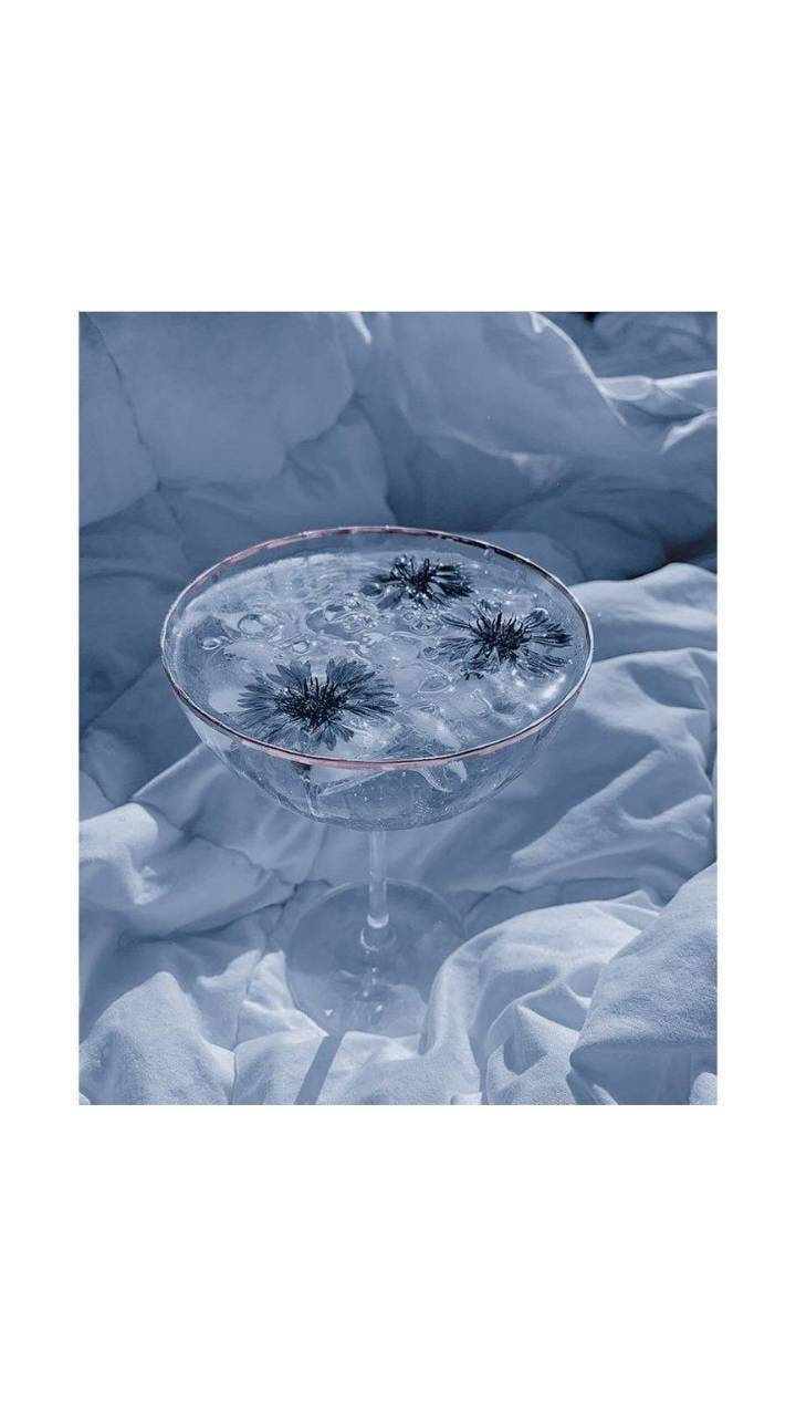 簡約藍色美學 桌布 壁紙 — 一個馬丁尼酒杯，內有漂浮的深色花朵，放在皺巴巴的淺藍色布料上，光線柔和清涼。