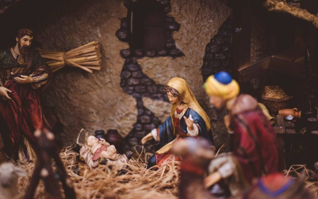 Nativity 桌布 壁紙 — 一個馬槽場景的特寫，有瑪利亞、約瑟和嬰兒耶穌的雕像，位於一個有稻草和石牆的質樸馬廄中。