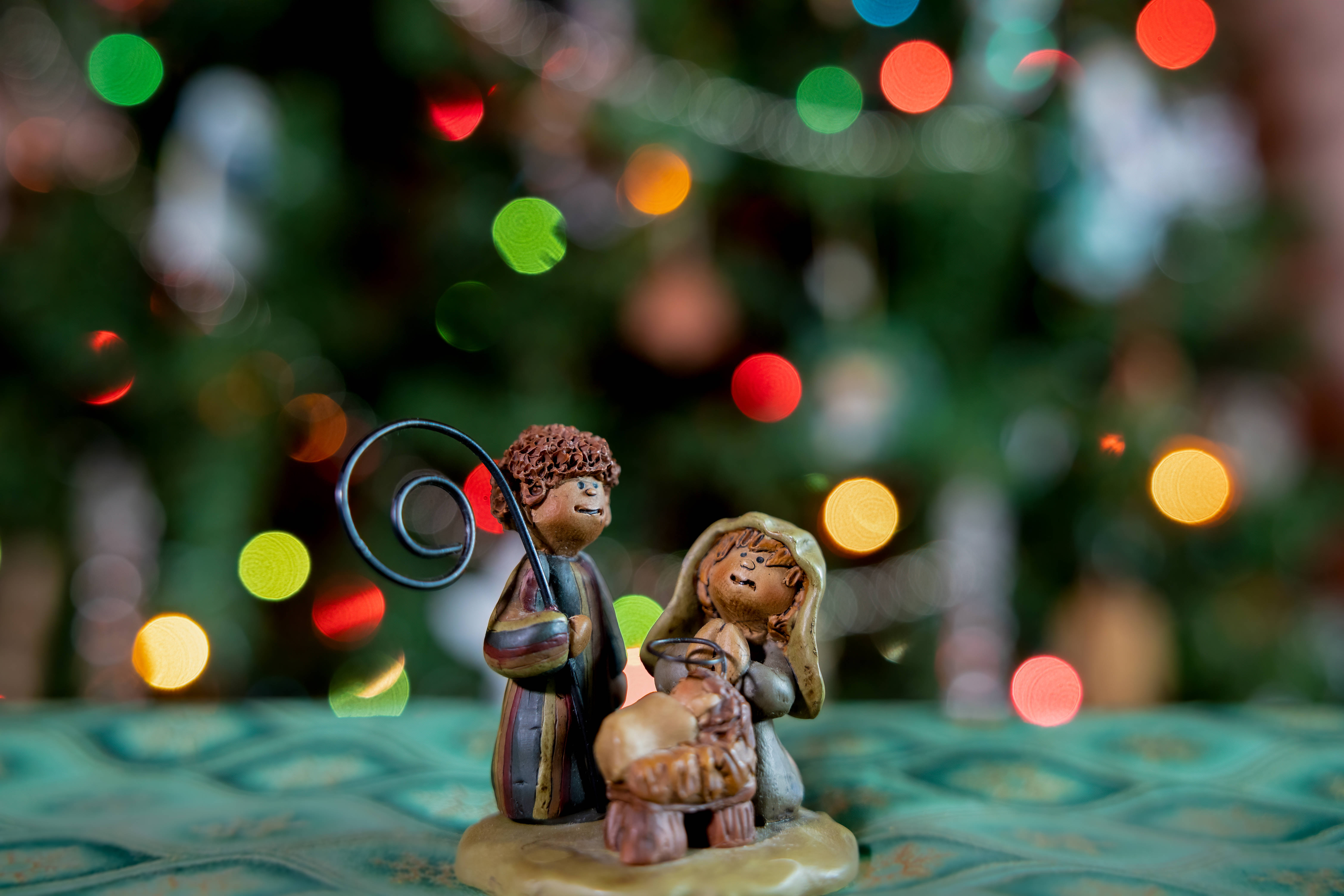 Nativity 桌布 壁紙 — 一個馬槽雕像的特寫，瑪利亞和約瑟抱著嬰兒耶穌，背景是色彩繽紛的聖誕燈光散景。