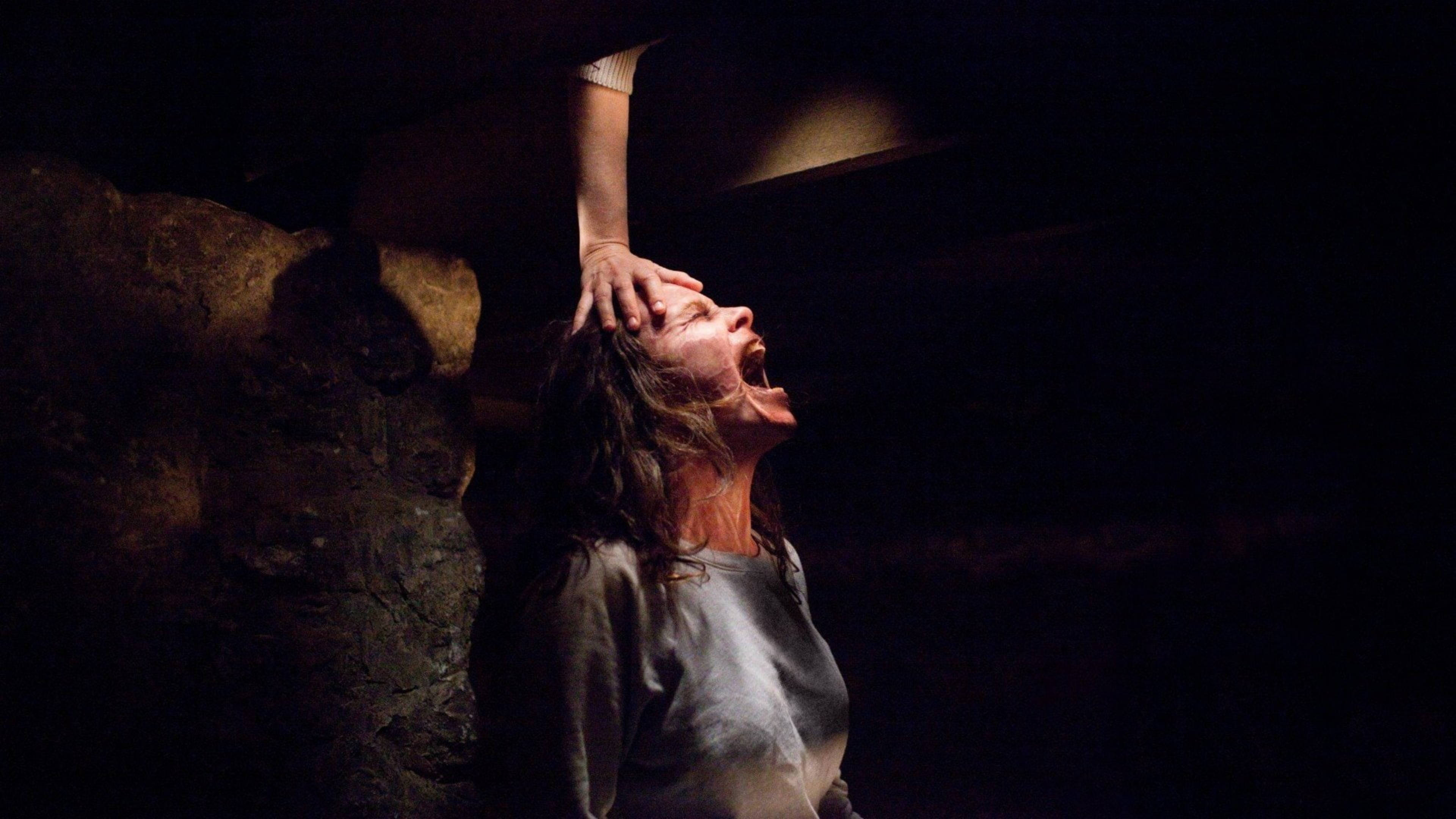 Conjuring 桌布 壁紙 — 一個驚恐的女人在黑暗、岩石洞穴中尖叫，一隻手壓在她的頭上。
