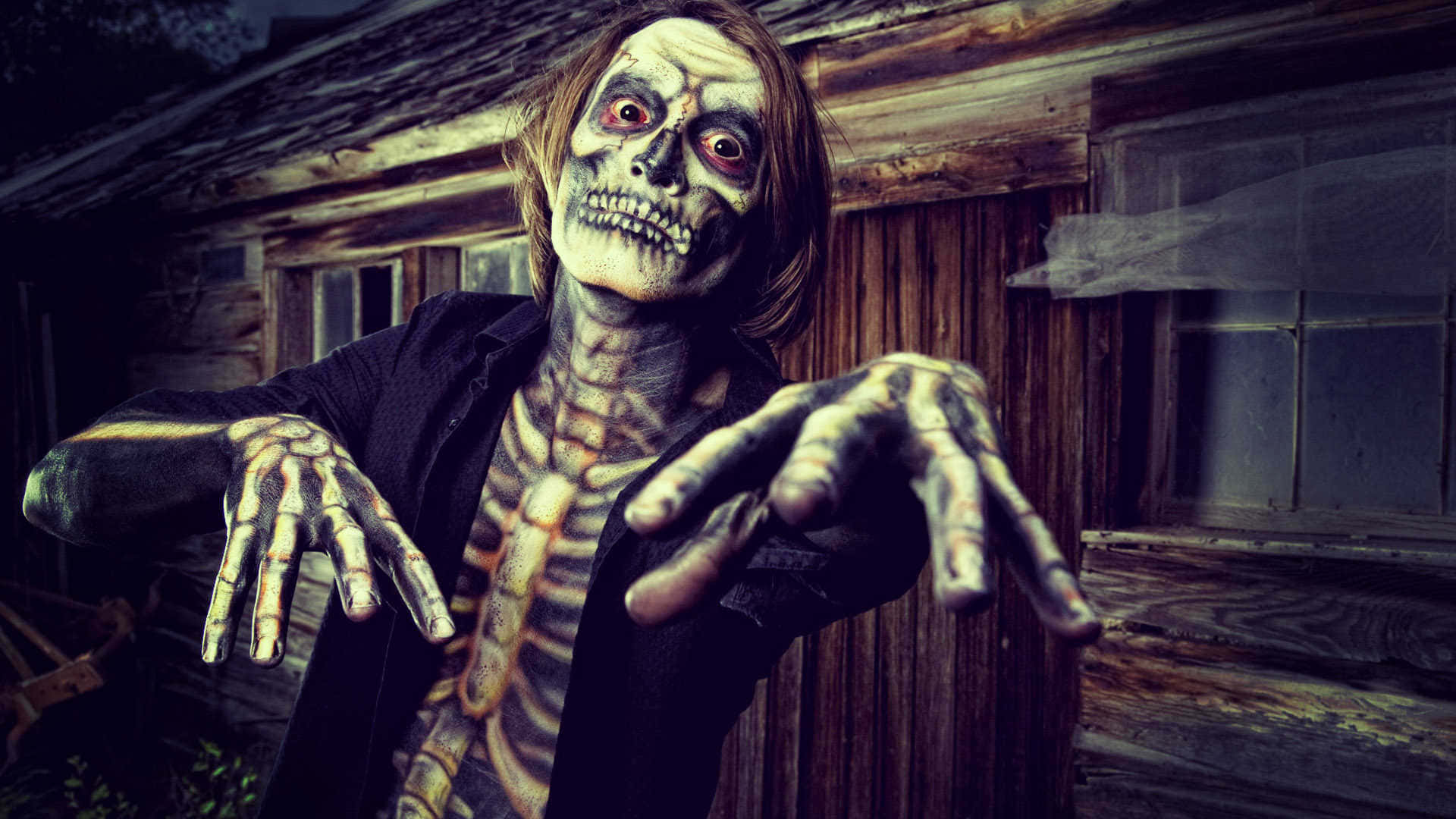 Horror Costumes 桌布 壁紙 — 一個骨骼恐怖角色，雙眼發出紅光，雙手伸出，從一間腐朽的木屋中威脅性地出現。
