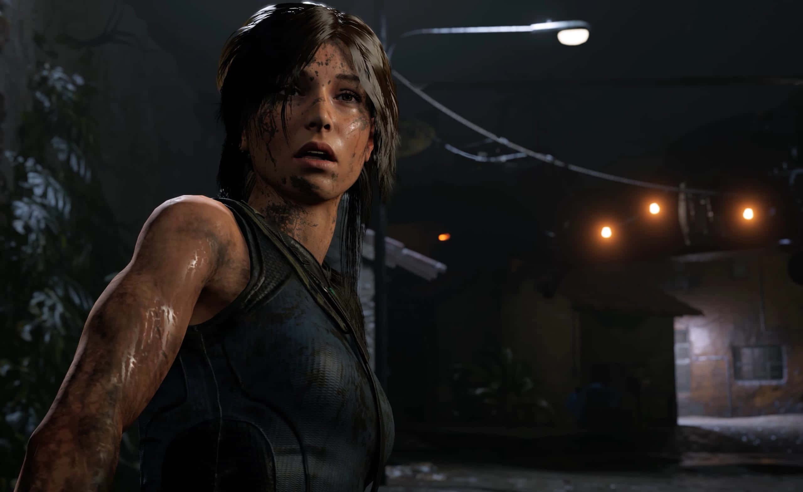 桌布 壁紙 — 一個骯髒且筋疲力盡的 Lara Croft 站在夜晚燈光昏暗的城市小巷中，街燈在潮濕的路面上投射出溫暖的光芒。